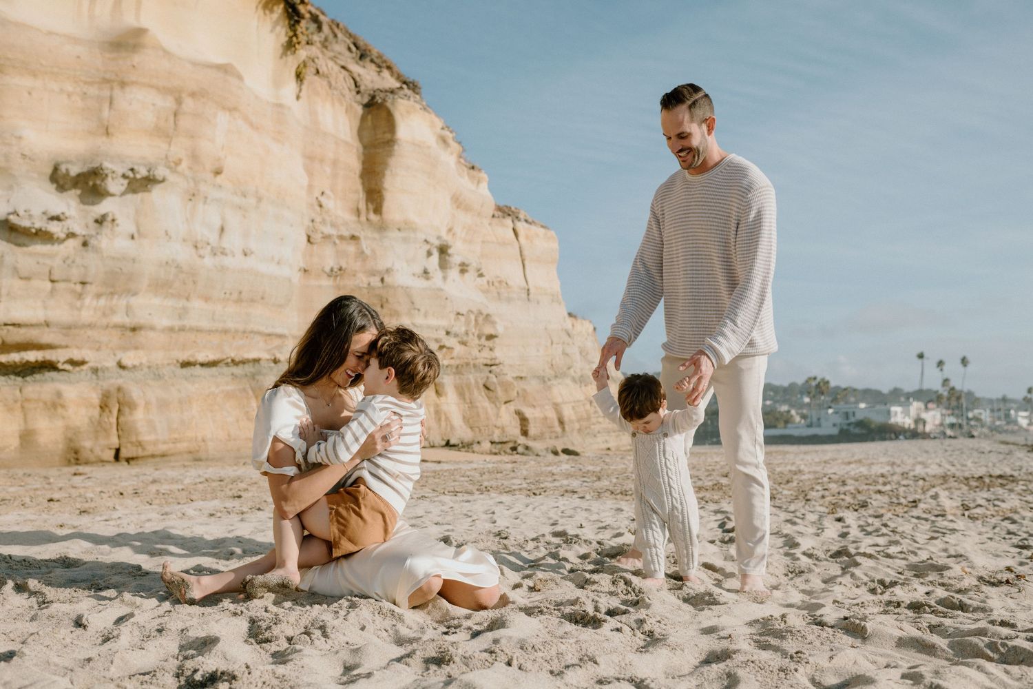 Family of four enjoying a sunny beach day with sandy cliffs backdrop.