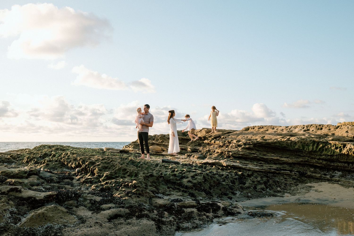 Family of four enjoying a romantic sunset photoshoot on rocky coastal shoreline.