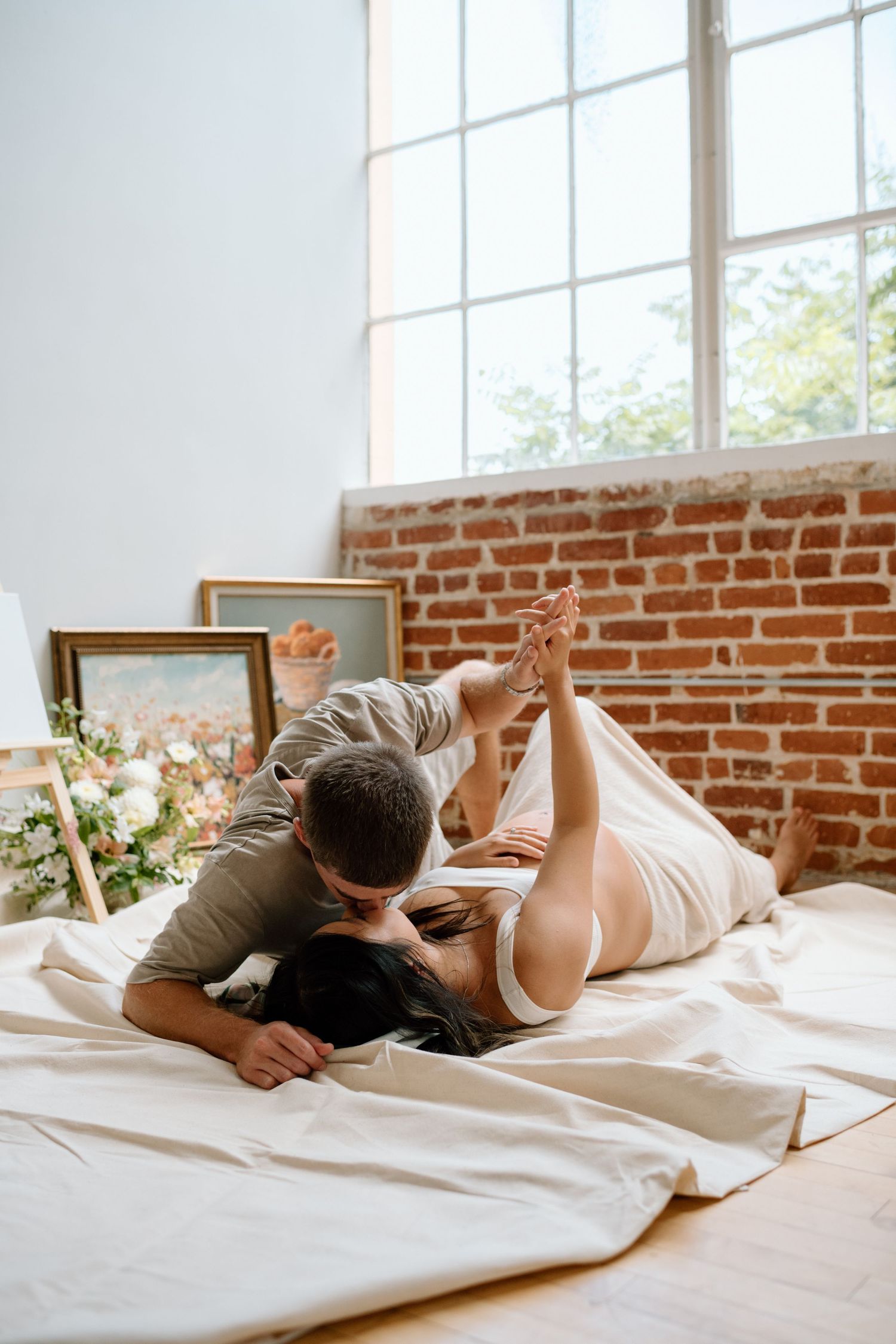 Man holds pregnant wifes hand while lying down during maternity photoshoot in a San Diego studio.