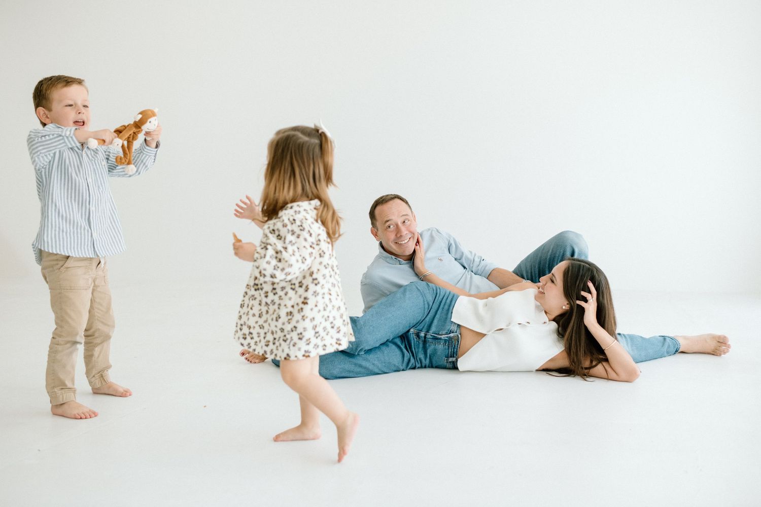 Playful family with two children and parents laughing on white studio floor.