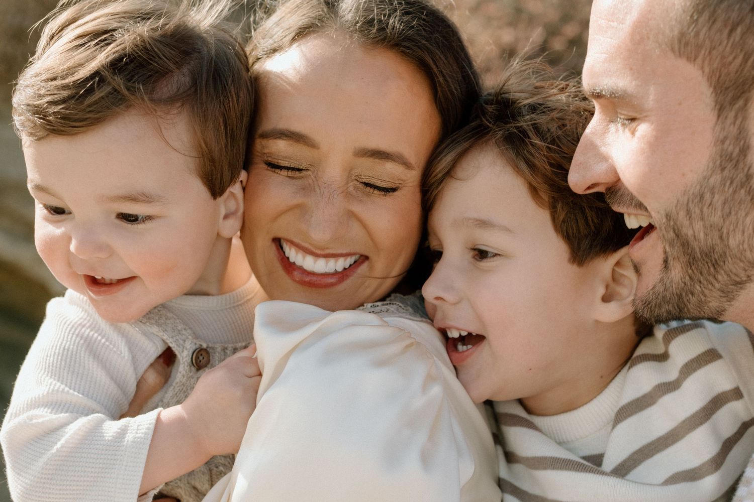 A joyful family of four shares a warm embrace, with two young boys snuggling close to their smiling parents.