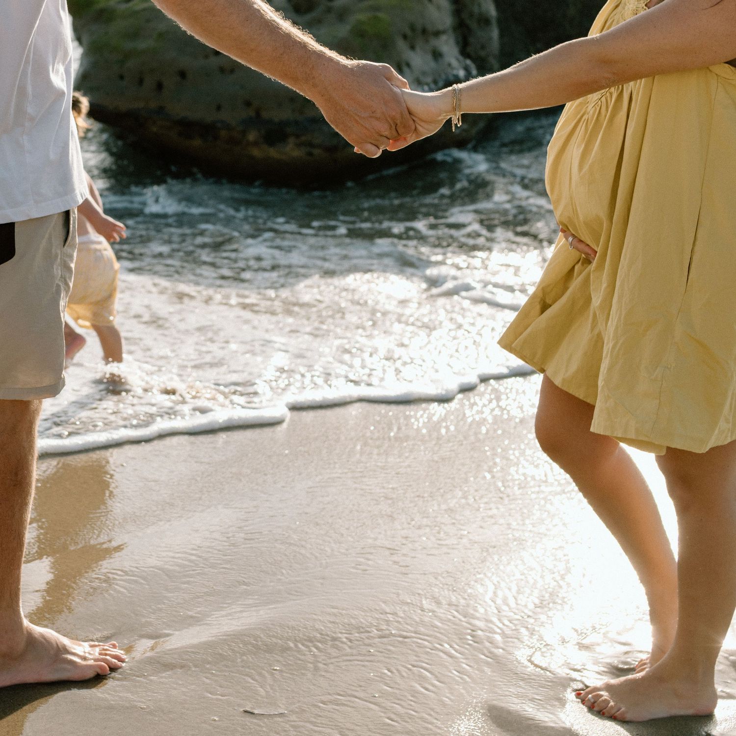 Couple holding hands barefoot on sandy beach near ocean waves.