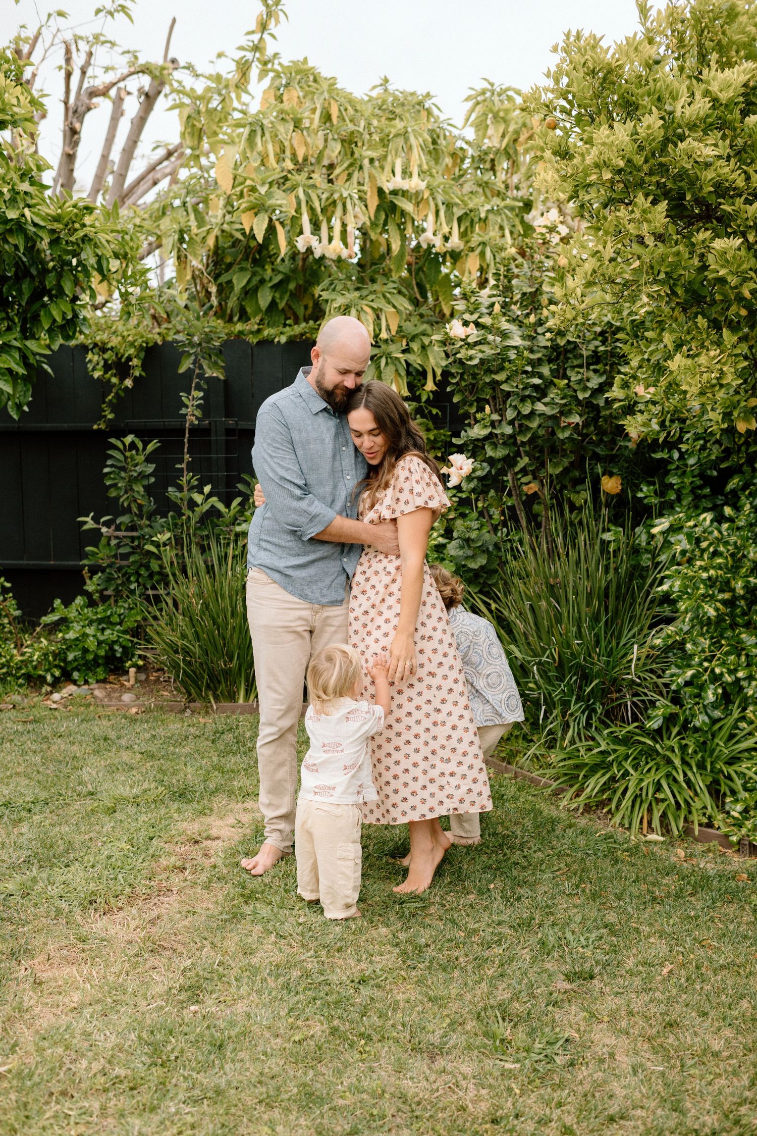 Couple with toddler sharing a tender family moment in a lush green backyard garden.