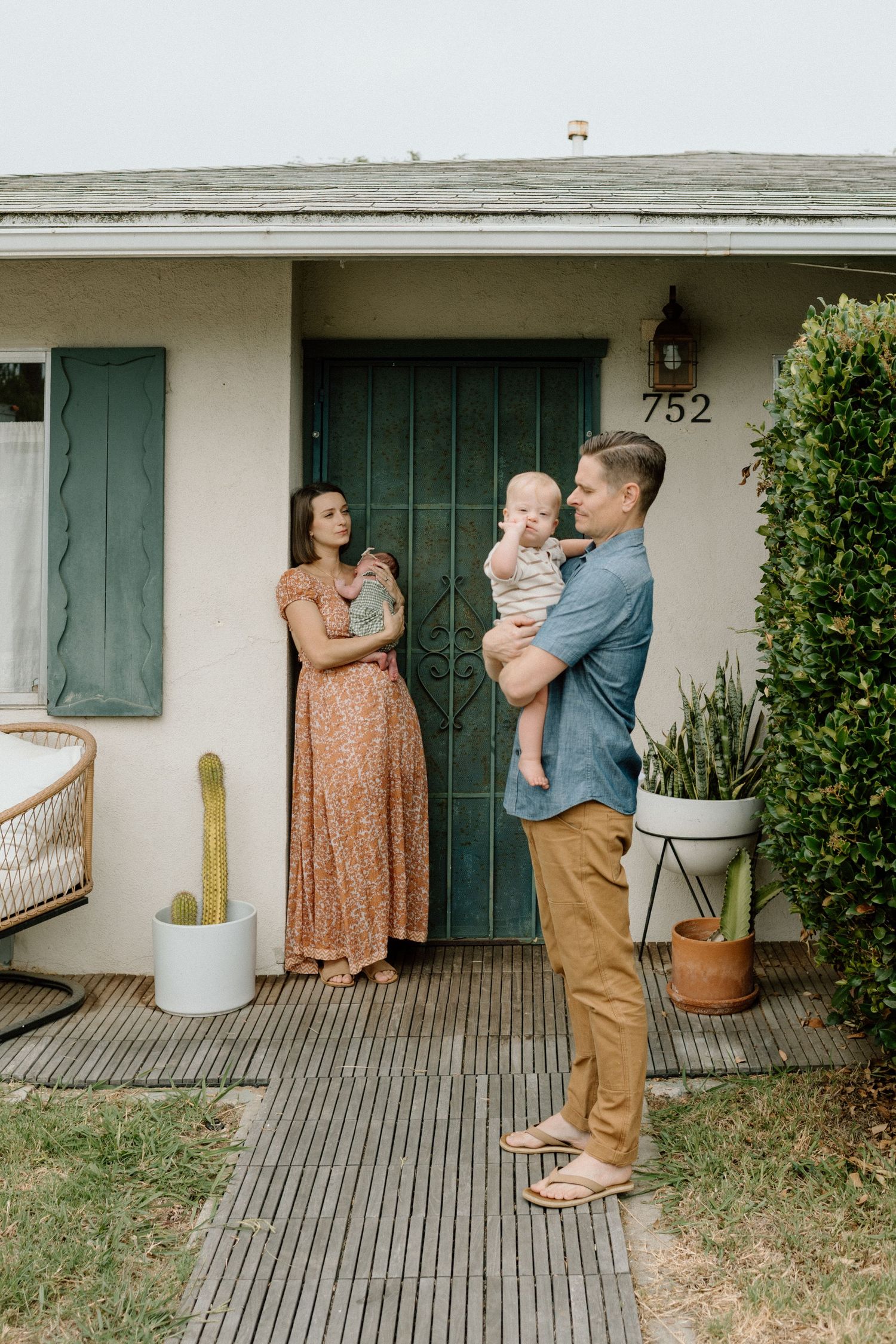 A young family stands outside their home at 752, with a woman in a floral dress and a man holding their baby.