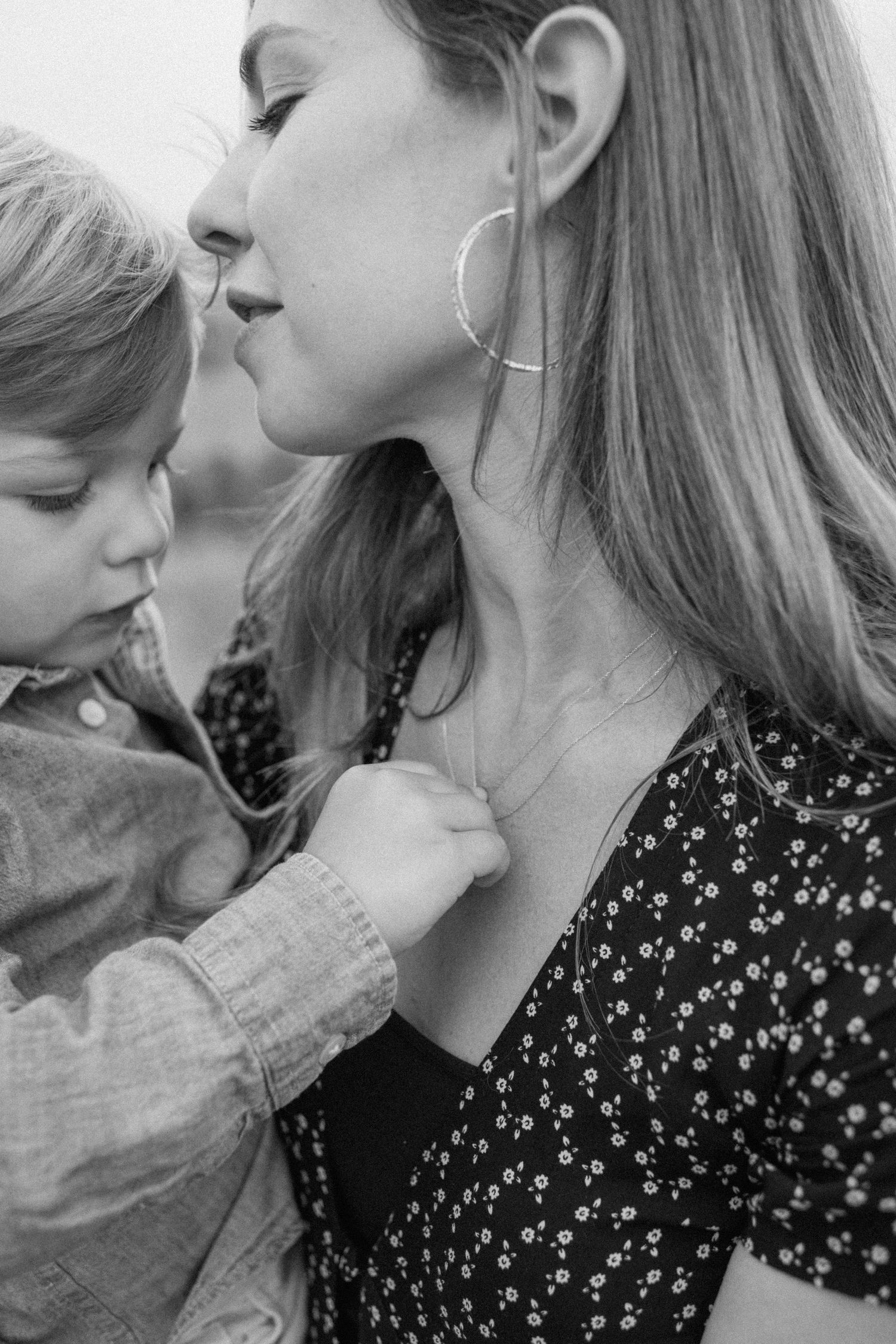 Close-up black and white portrait of mother holding young child who gently touches her necklace.