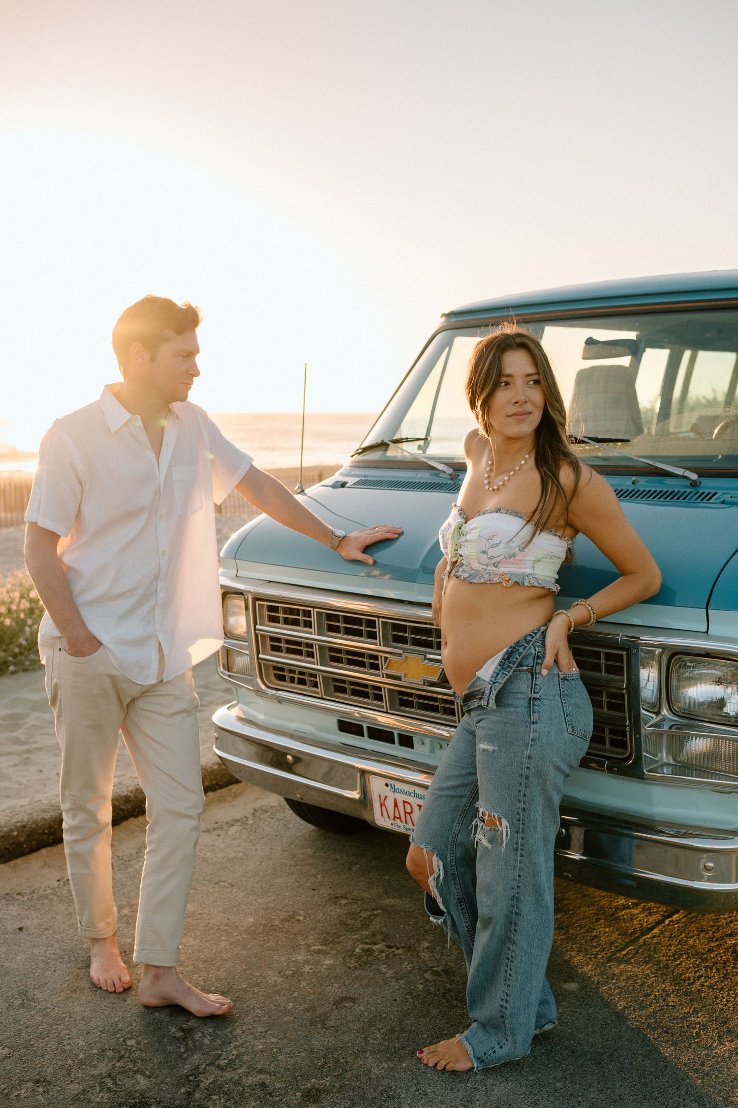 Couple posing in front of a vintage blue Chevrolet truck at sunset near the beach.