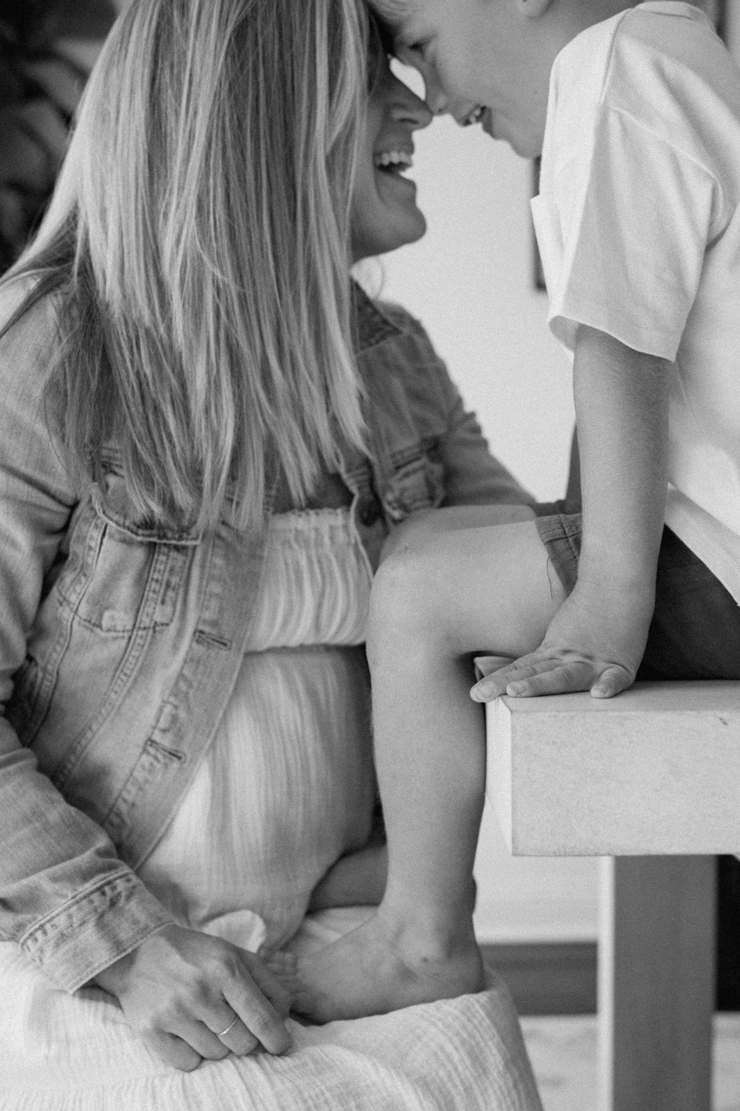Black and white photo of a laughing pregnant woman sharing a tender nose-to-nose moment with her child.