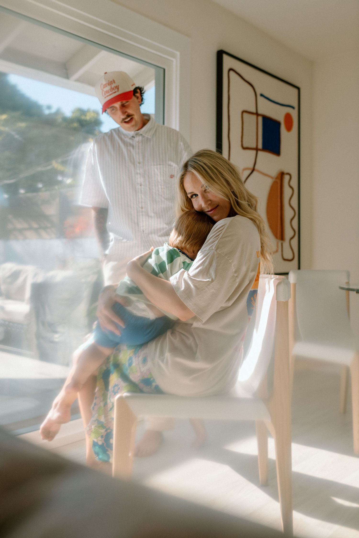 Sunlit room with two people and modern abstract wall art, creating a warm domestic atmosphere in soft morning light.