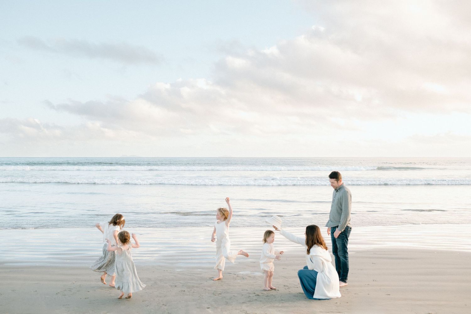 A joyful family plays on a serene beach at sunset, with children dancing near the ocean waves.