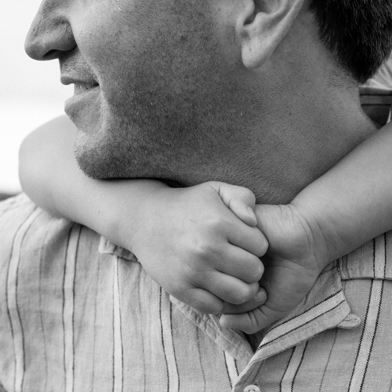 A black and white close-up of a child wrapping small arms around a fathers neck.