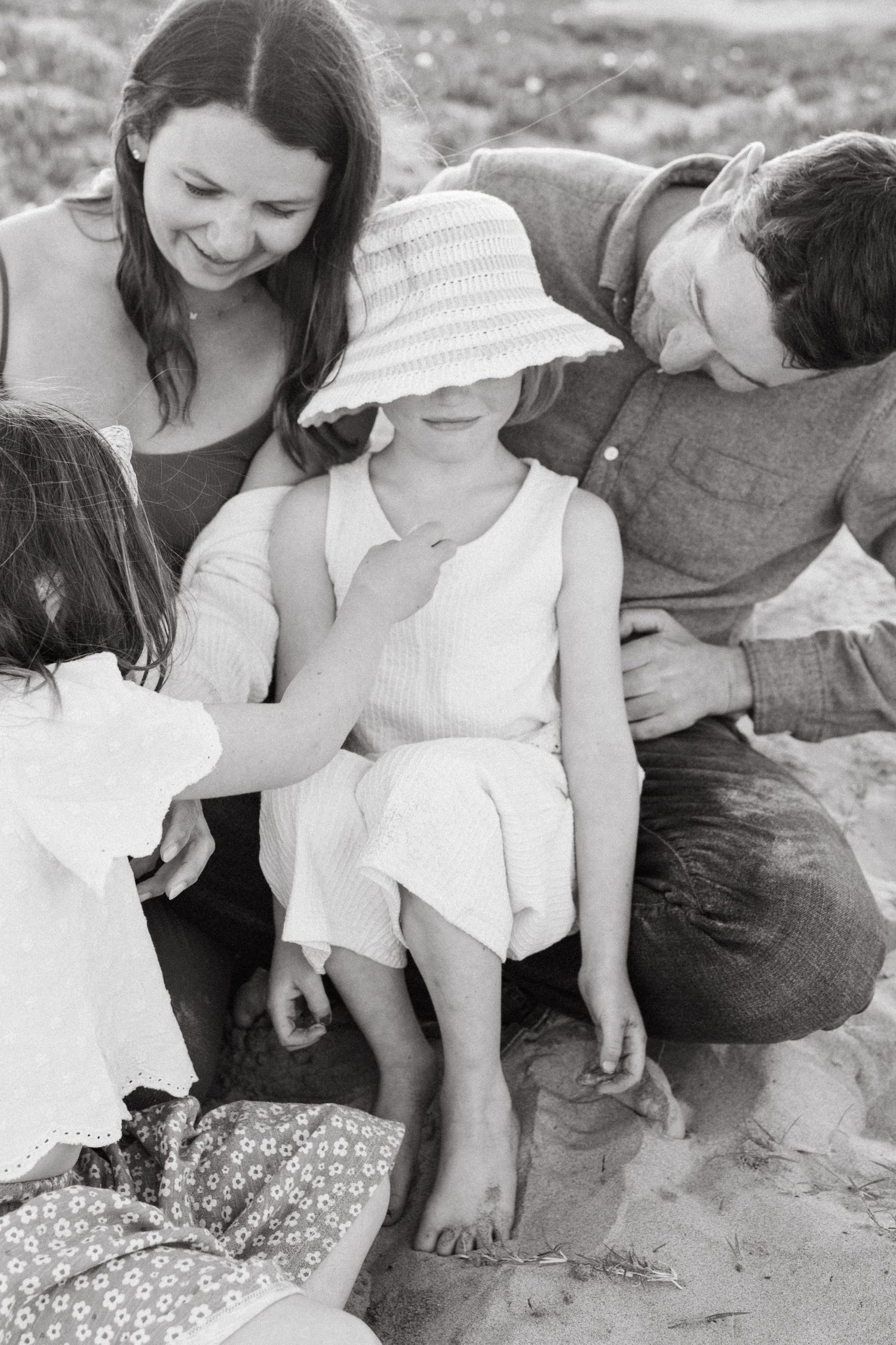 Black and white beach photo of parents and two daughters playing together in sand.