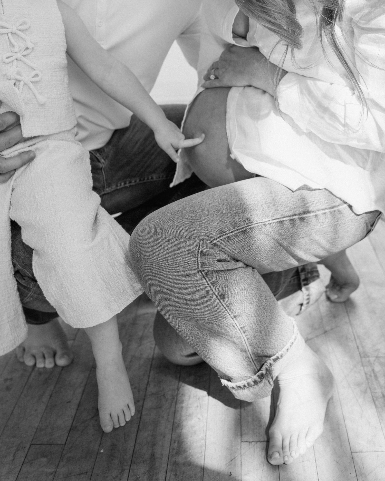 Black and white overhead shot of a pregnant woman and children on a wooden floor.