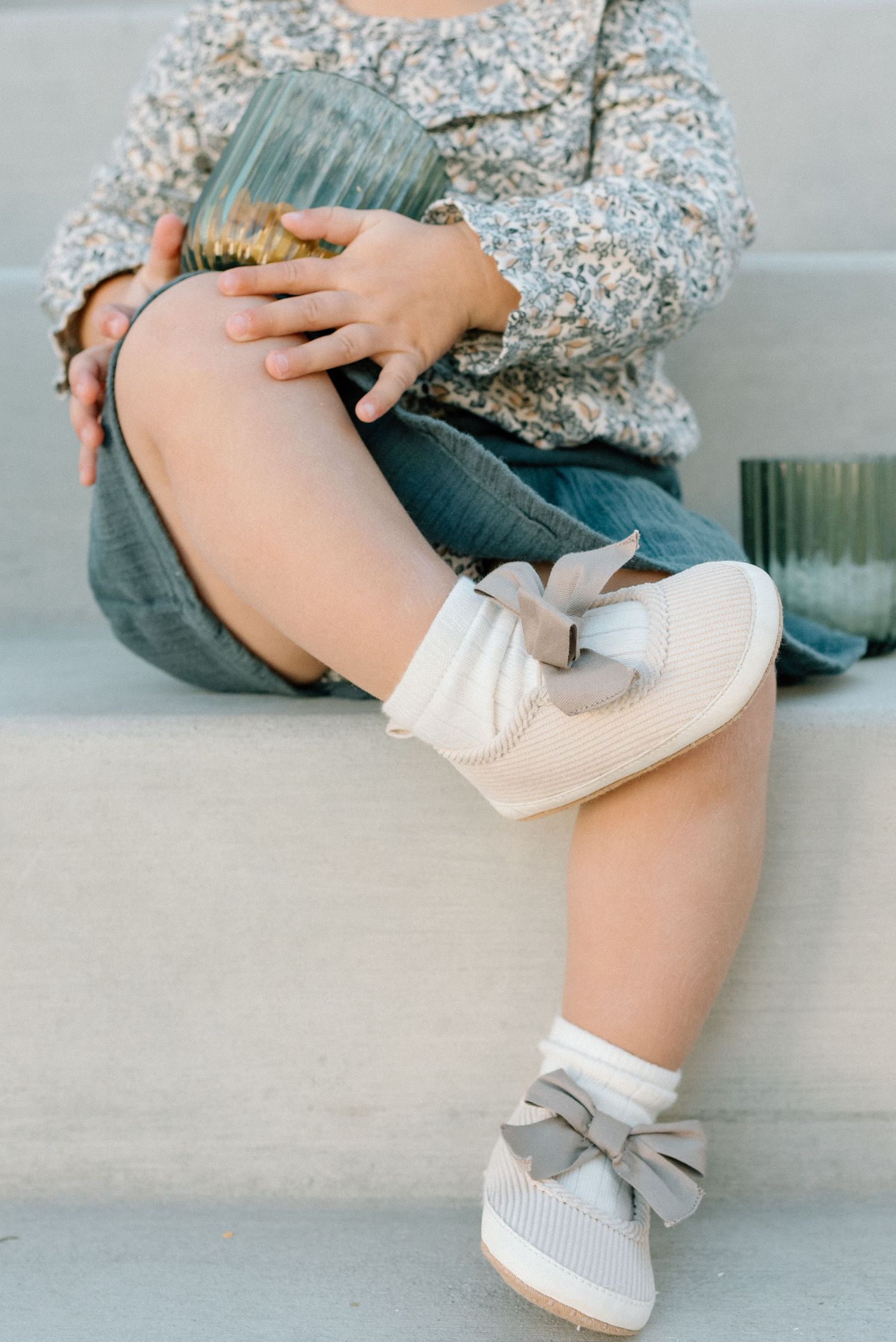 Toddler wearing cream bow shoes and white socks sitting on steps.