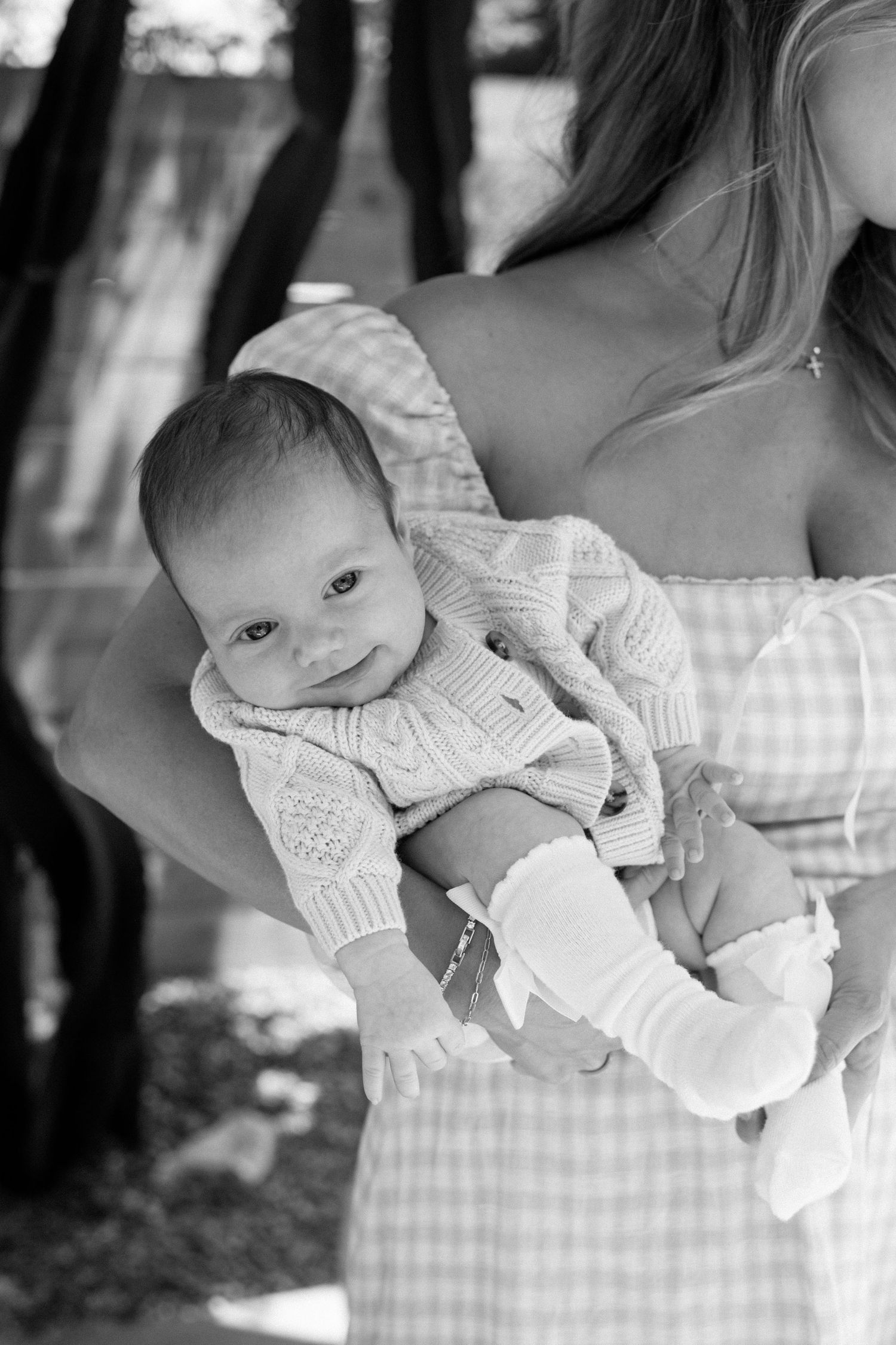 Black and white photo of a mother holding her smiling newborn baby outdoors.