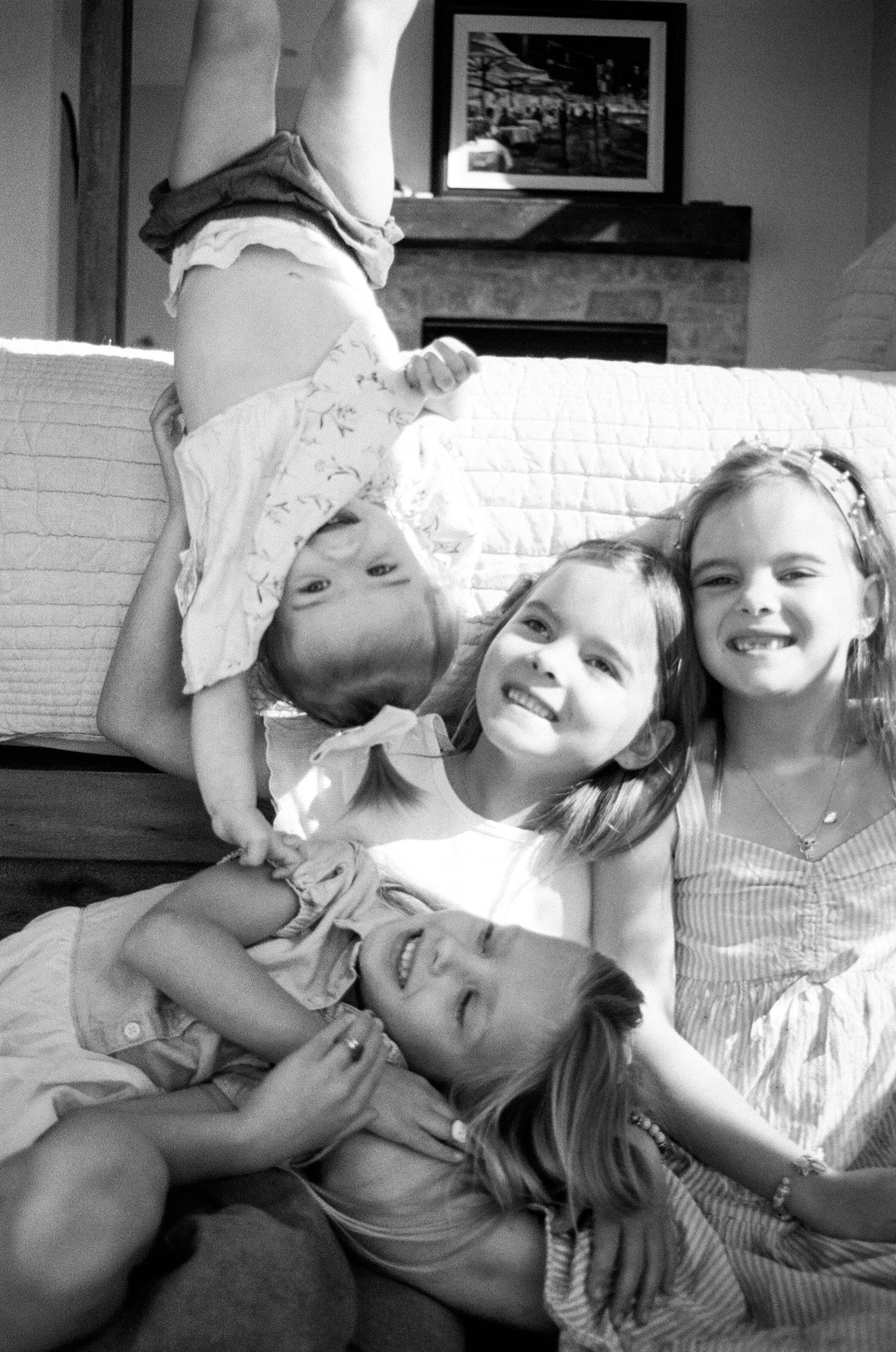 Black and white photo of four young sisters laughing and piling together on a bed playfully.
