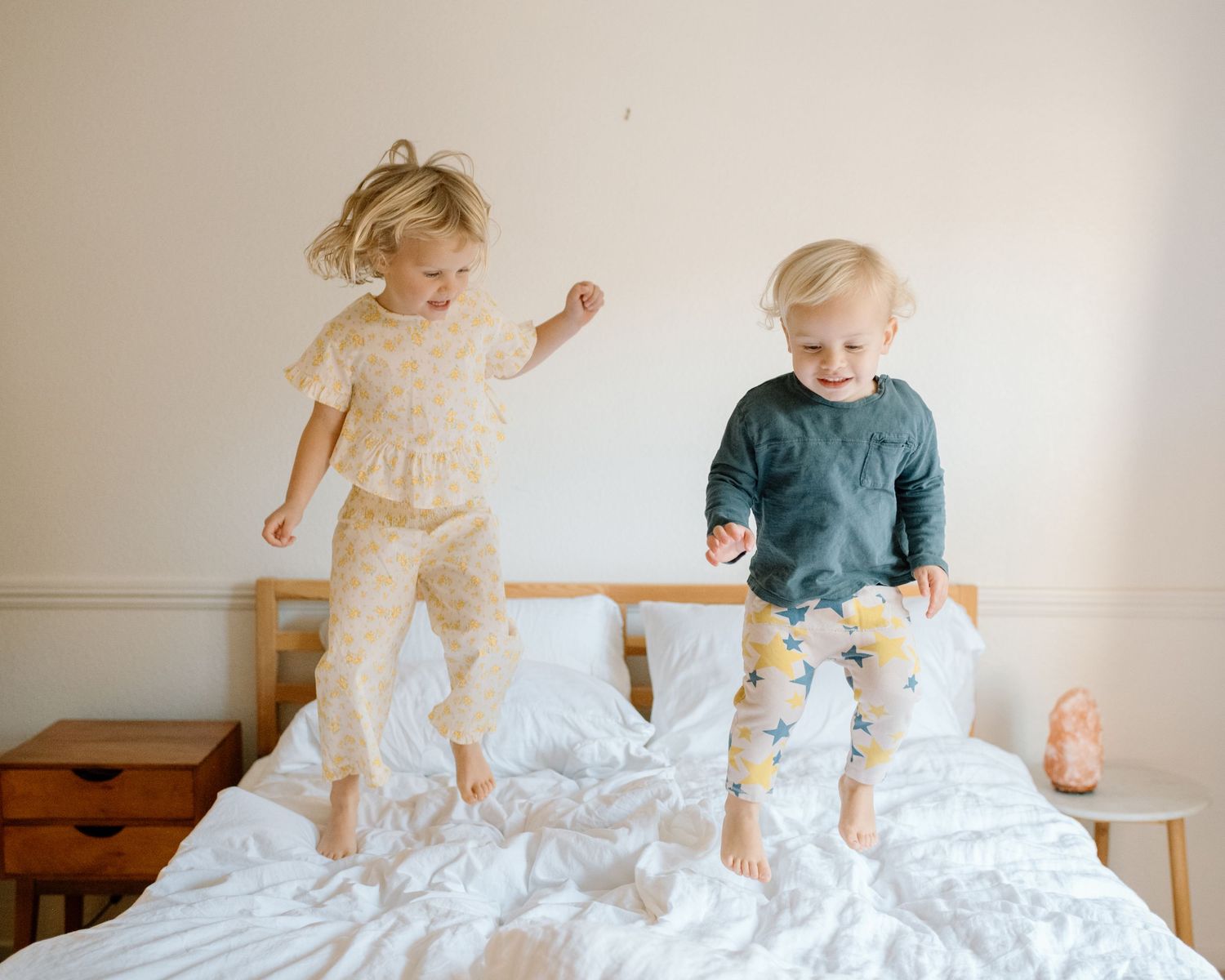 Two young children joyfully jumping on a white bed in bright matching pajamas indoors.