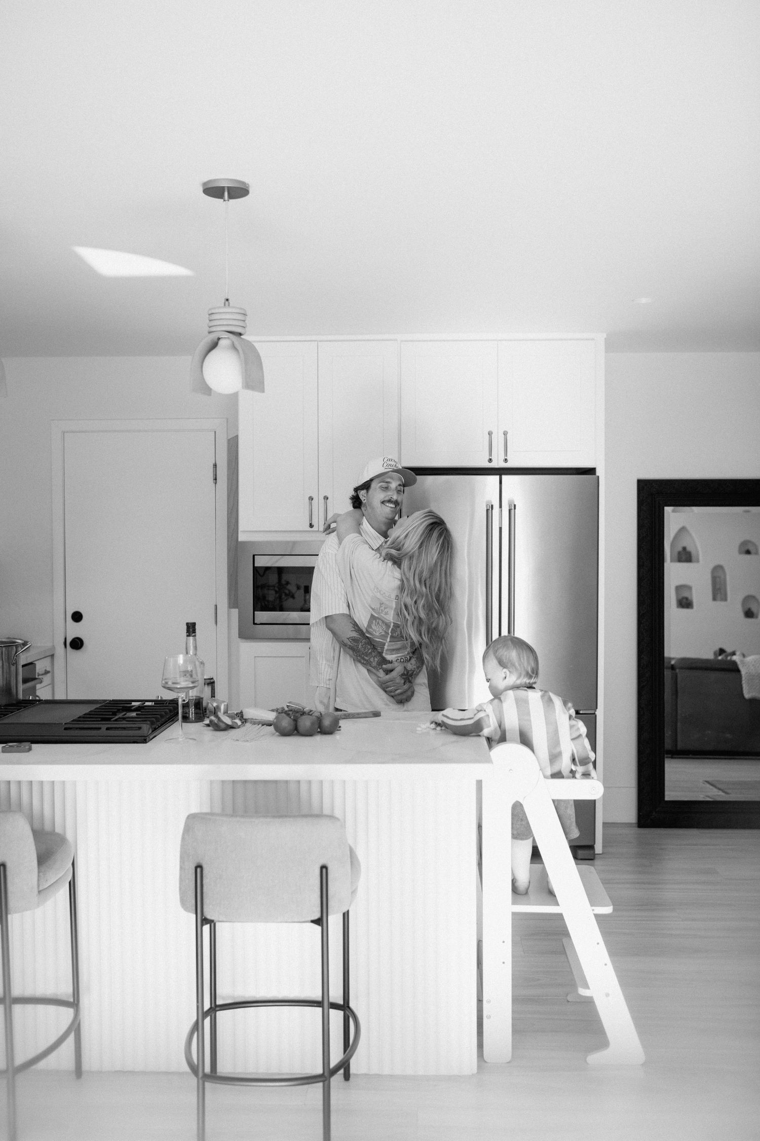 A sequence of six black and white photos showing meal preparation and activities in a minimalist kitchen with white cabinets.