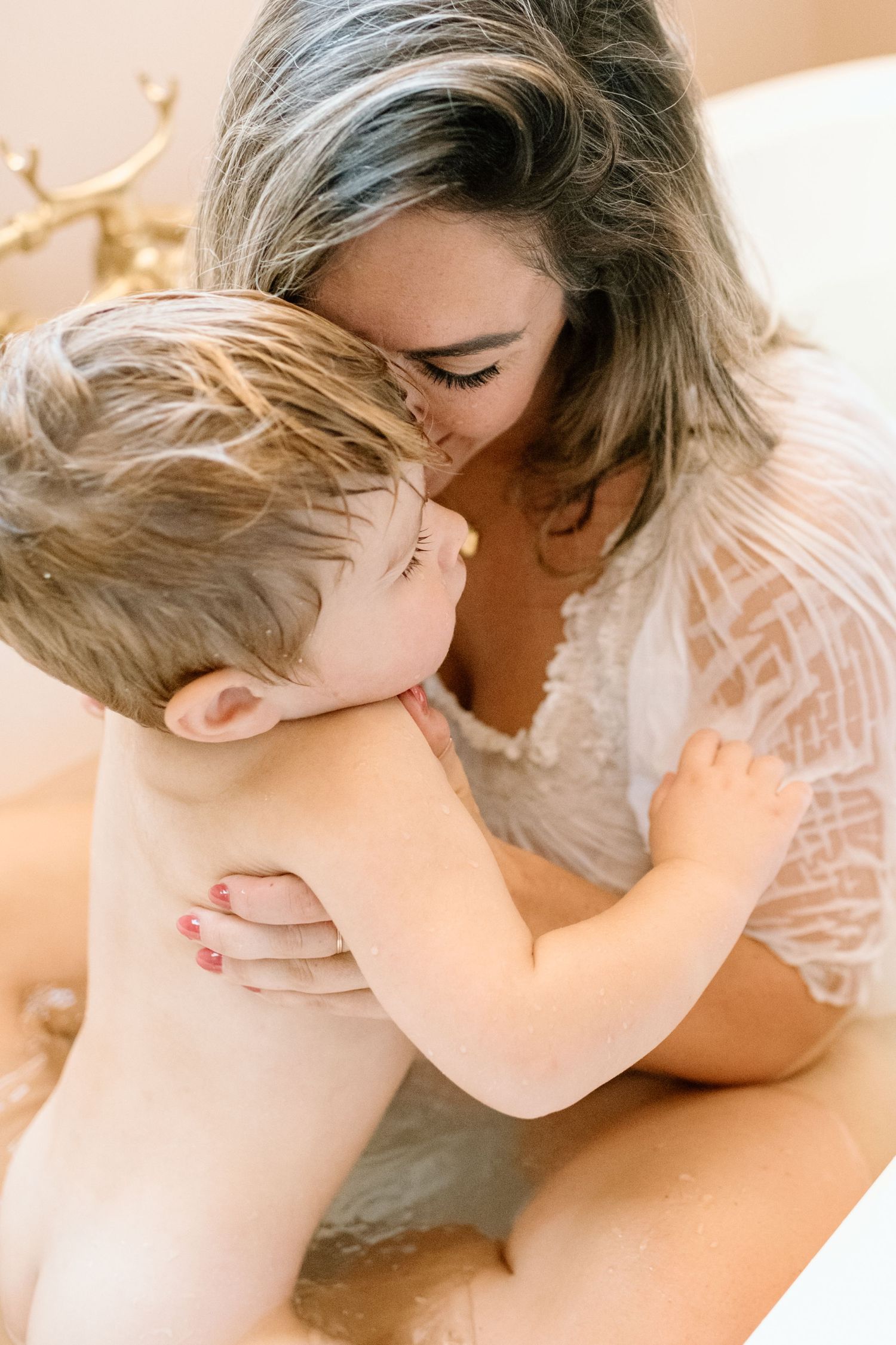A mother tenderly kisses her baby while holding them close in a warm, softly lit setting.