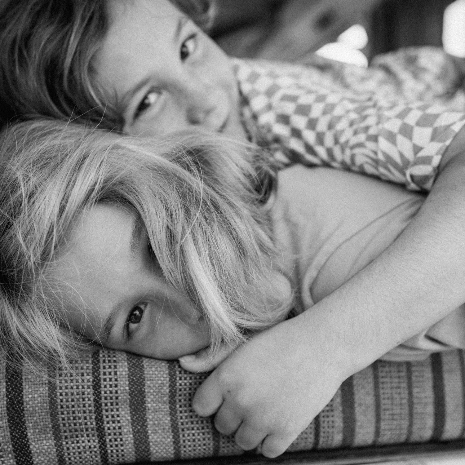 Black and white close-up of two young blonde children cuddling together on a striped cushion.