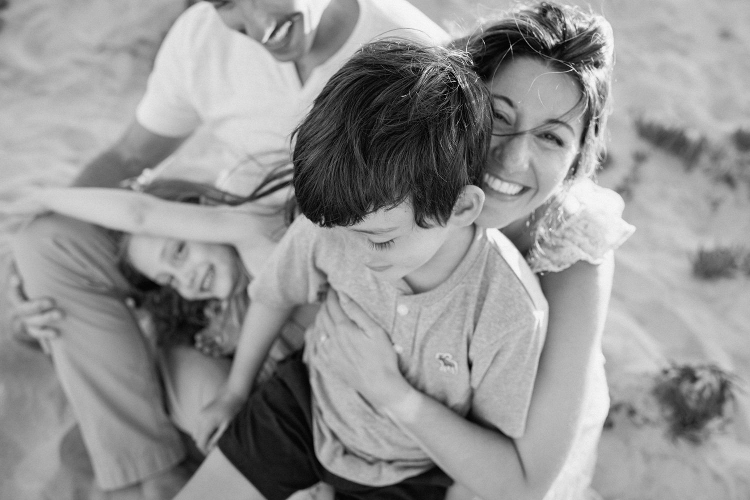 Black and white photo of a smiling family with two children playing together on a sandy beach.