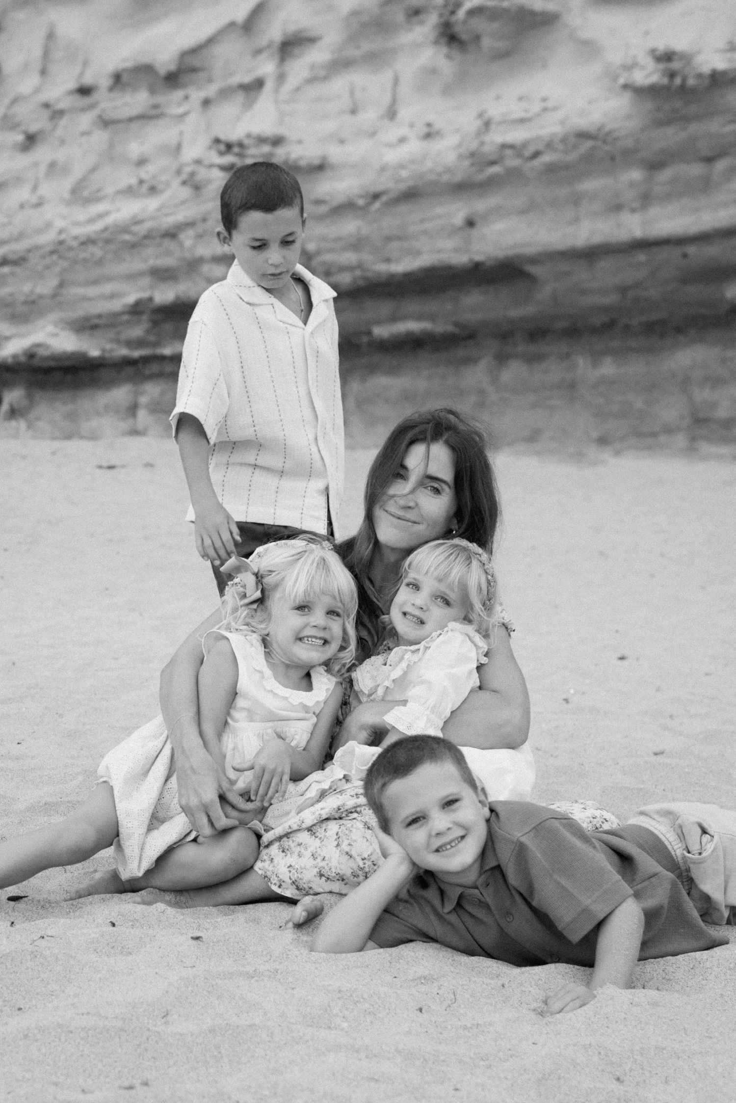 Black and white beach photo of smiling mother surrounded by four happy children.