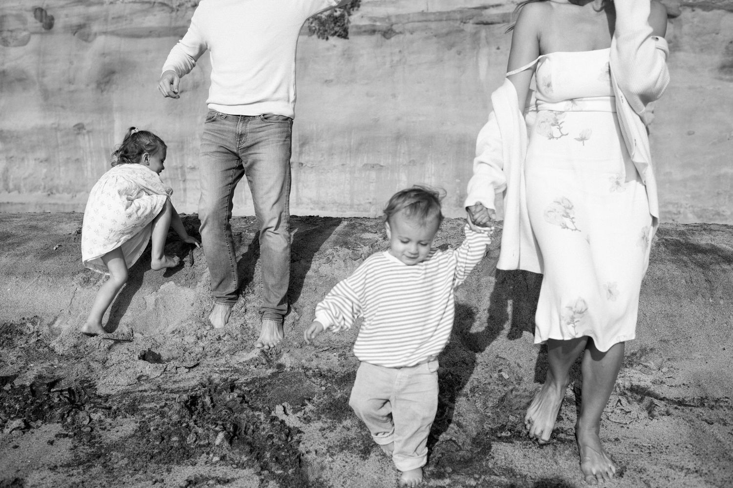 Family walking barefoot on sandy beach in black and white photo, children playing in sand.