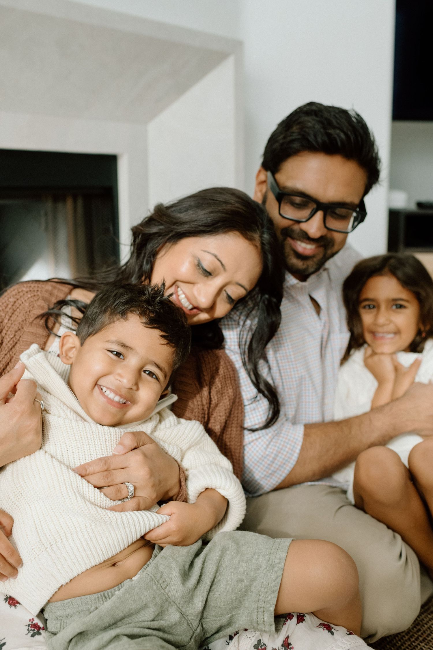 Happy South Asian family of four cuddling together indoors.