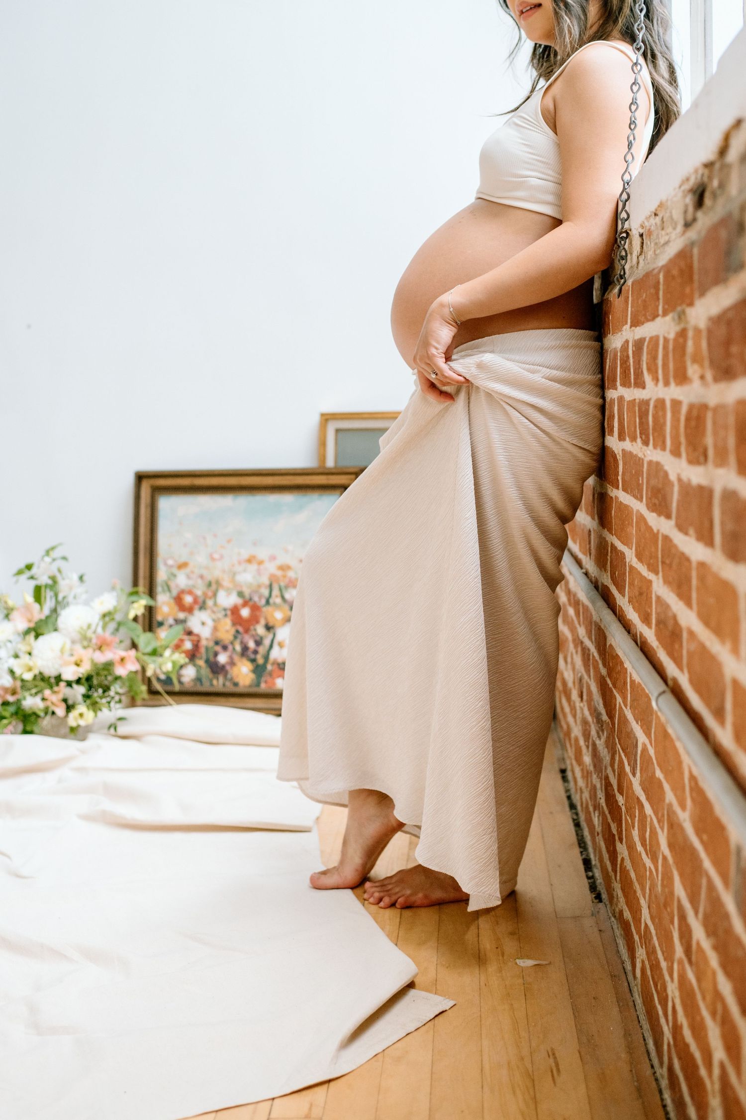 Pregnant woman leans against wall during maternity photoshoot in a San Diego studio.