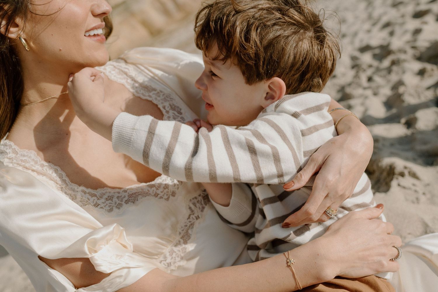 Mother tenderly embracing young boy on a sunny beach.