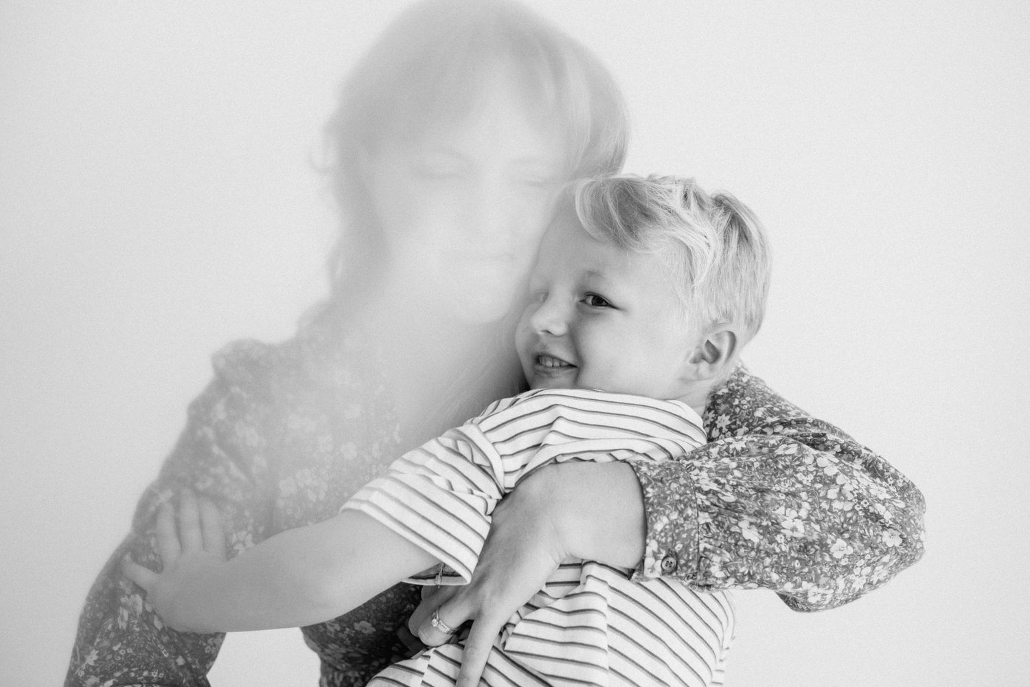 Black and white photo of a smiling toddler being lovingly embraced by a woman in a sparkly outfit.