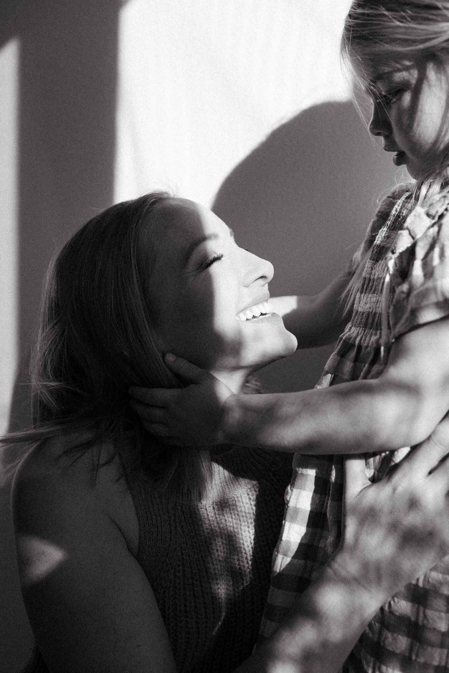 Black and white photo of a smiling mother gazing up at her young child holding her face tenderly.