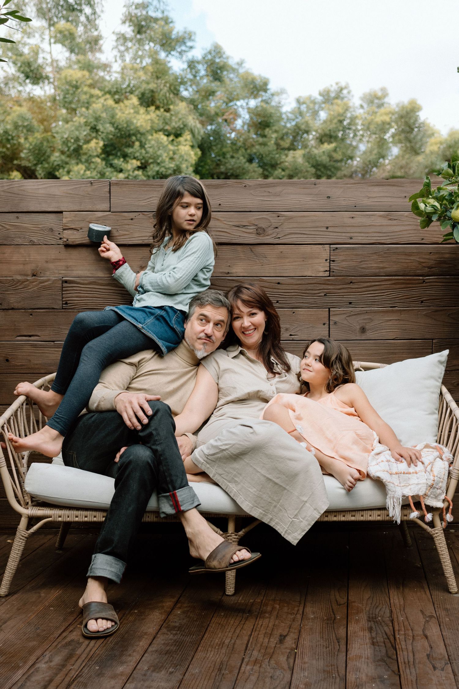 Family of four relaxing together on outdoor patio sofa against rustic wooden wall.