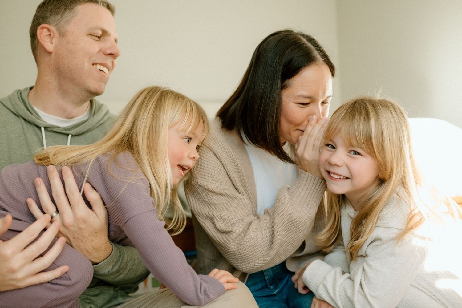 Joyful family of four laughing and playing together on a bright cozy couch indoors.