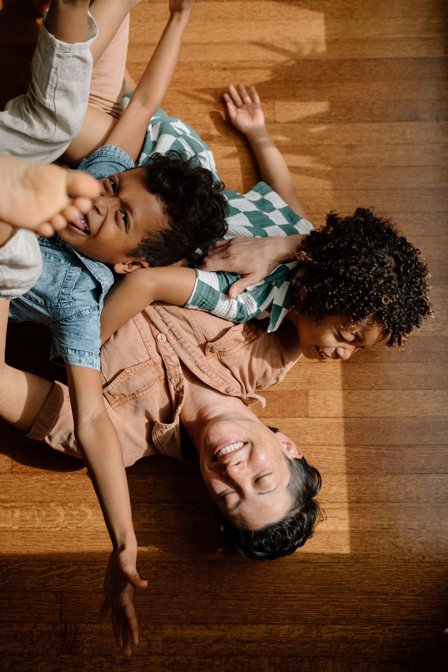Overhead view of a laughing mother lying on hardwood floor with two children piled on top of her.