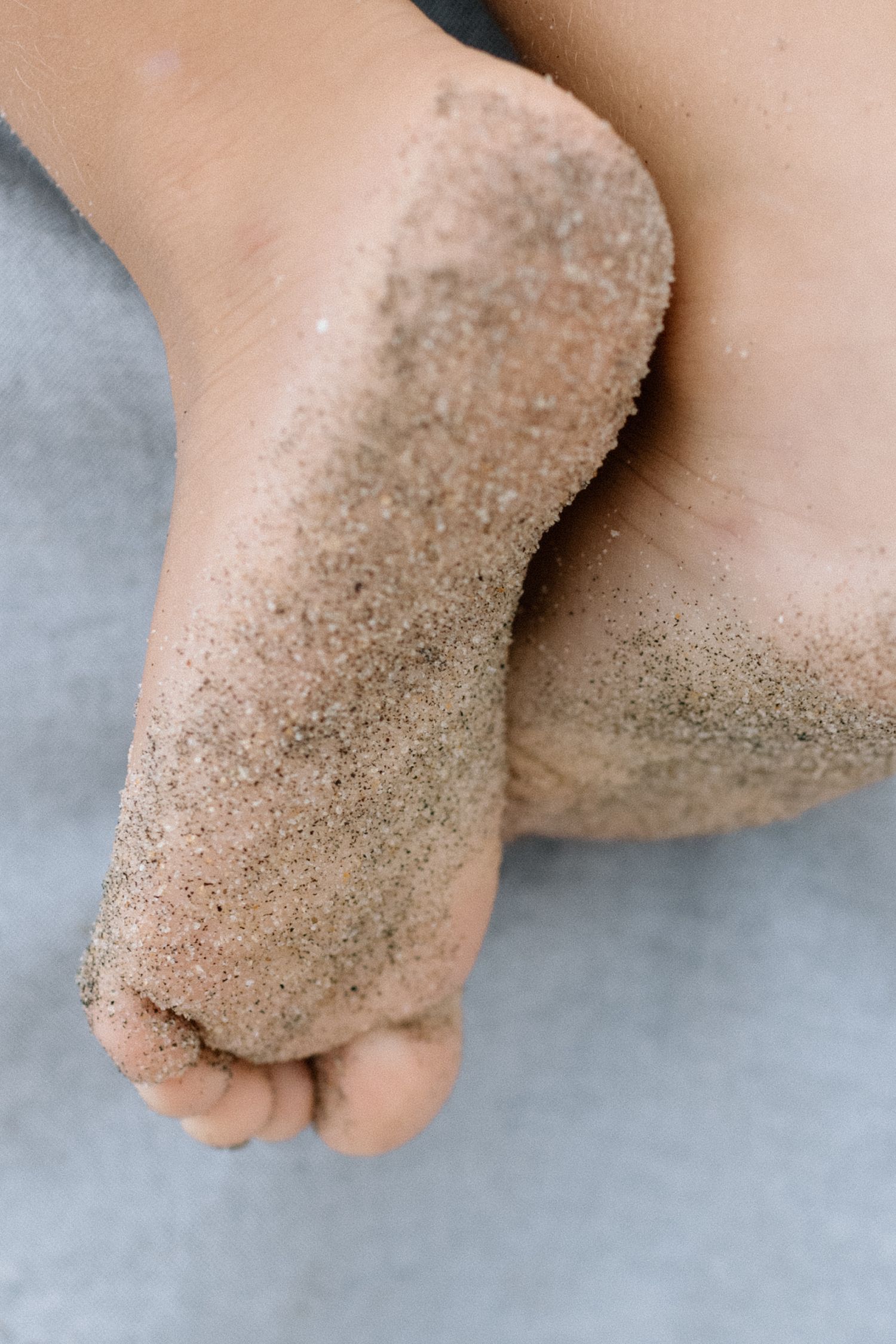 Close-up of sandy feet at the beach, covered in fine golden sand.