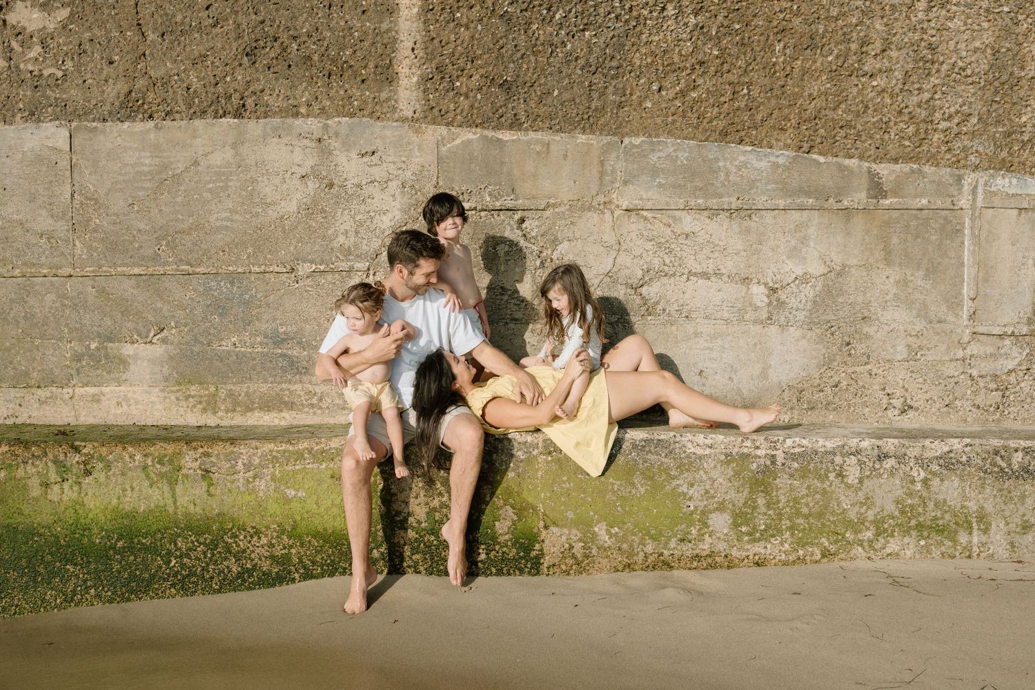 Family relaxing together on a stone ledge at the beach on a sunny day.