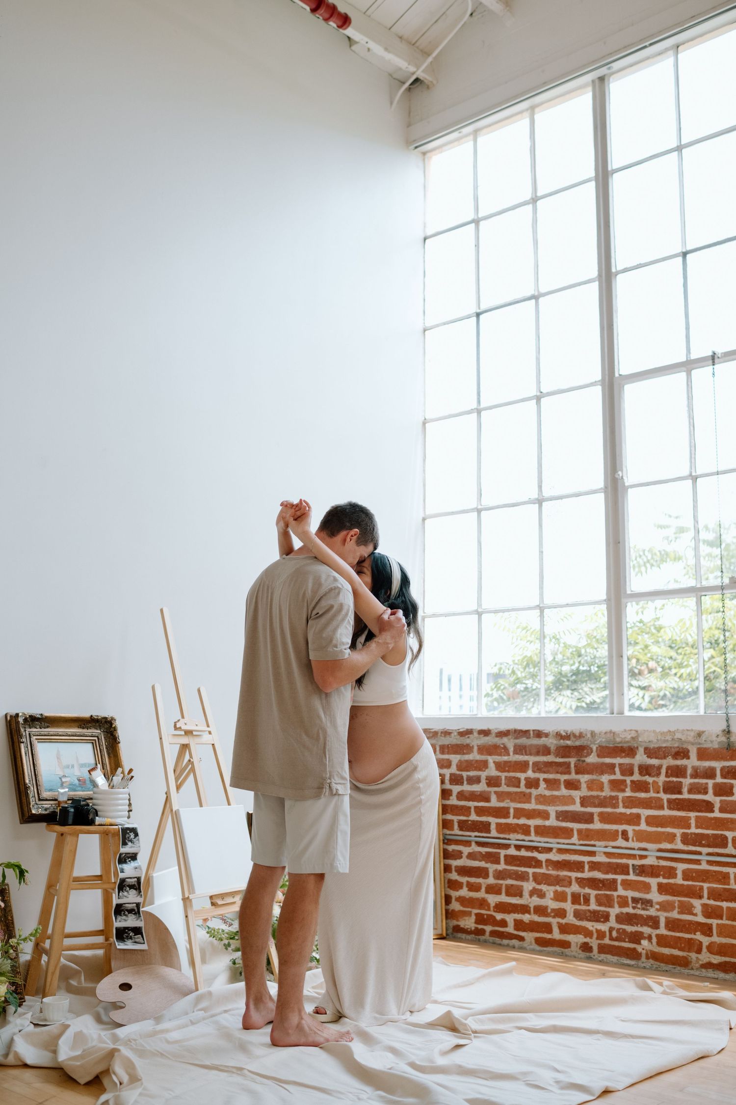Standing man embraces pregnant wife during maternity photoshoot in a San Diego studio.
