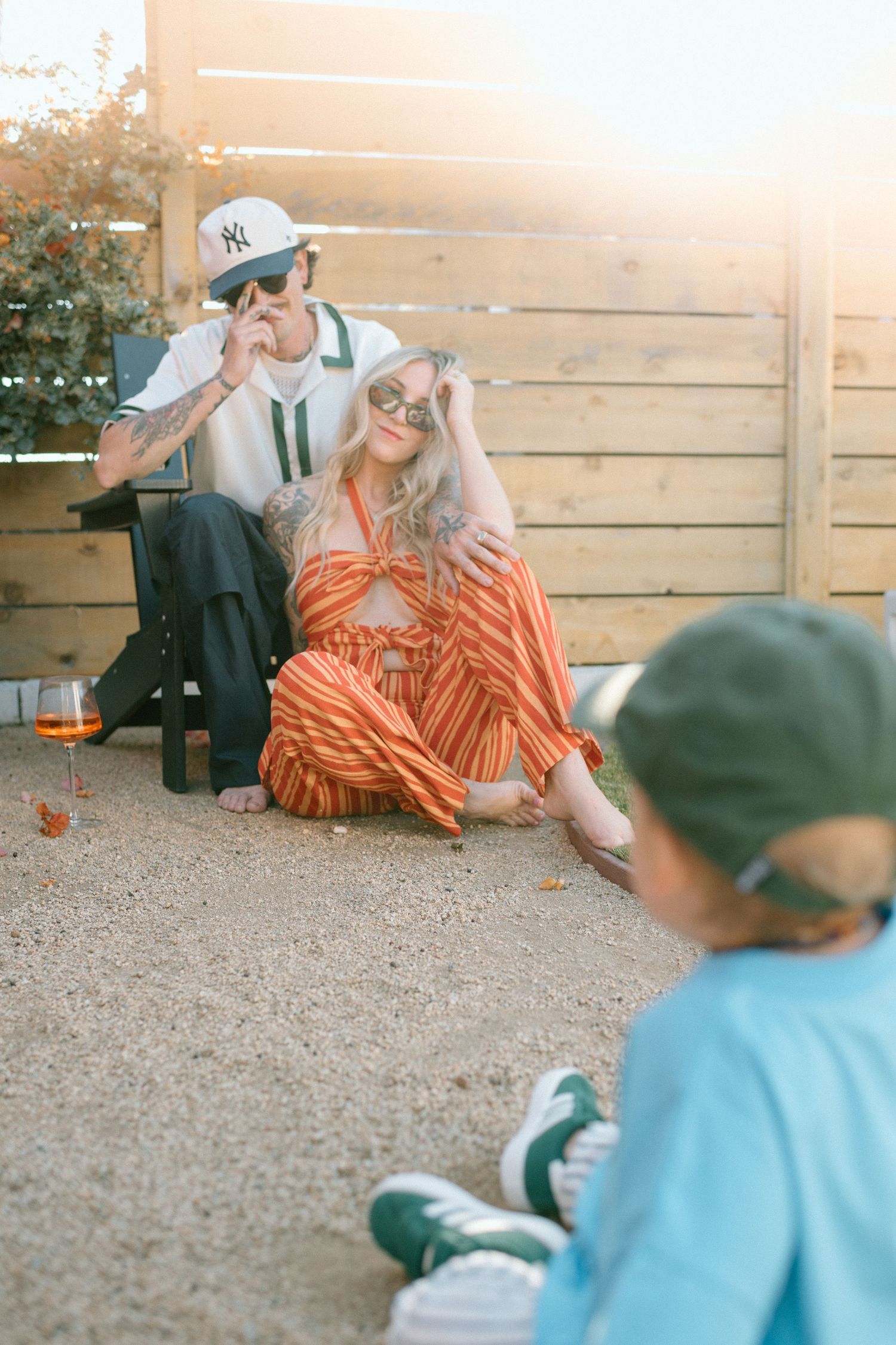 A family relaxes outdoors on a warm evening with a wooden fence backdrop and glowing sunset light.