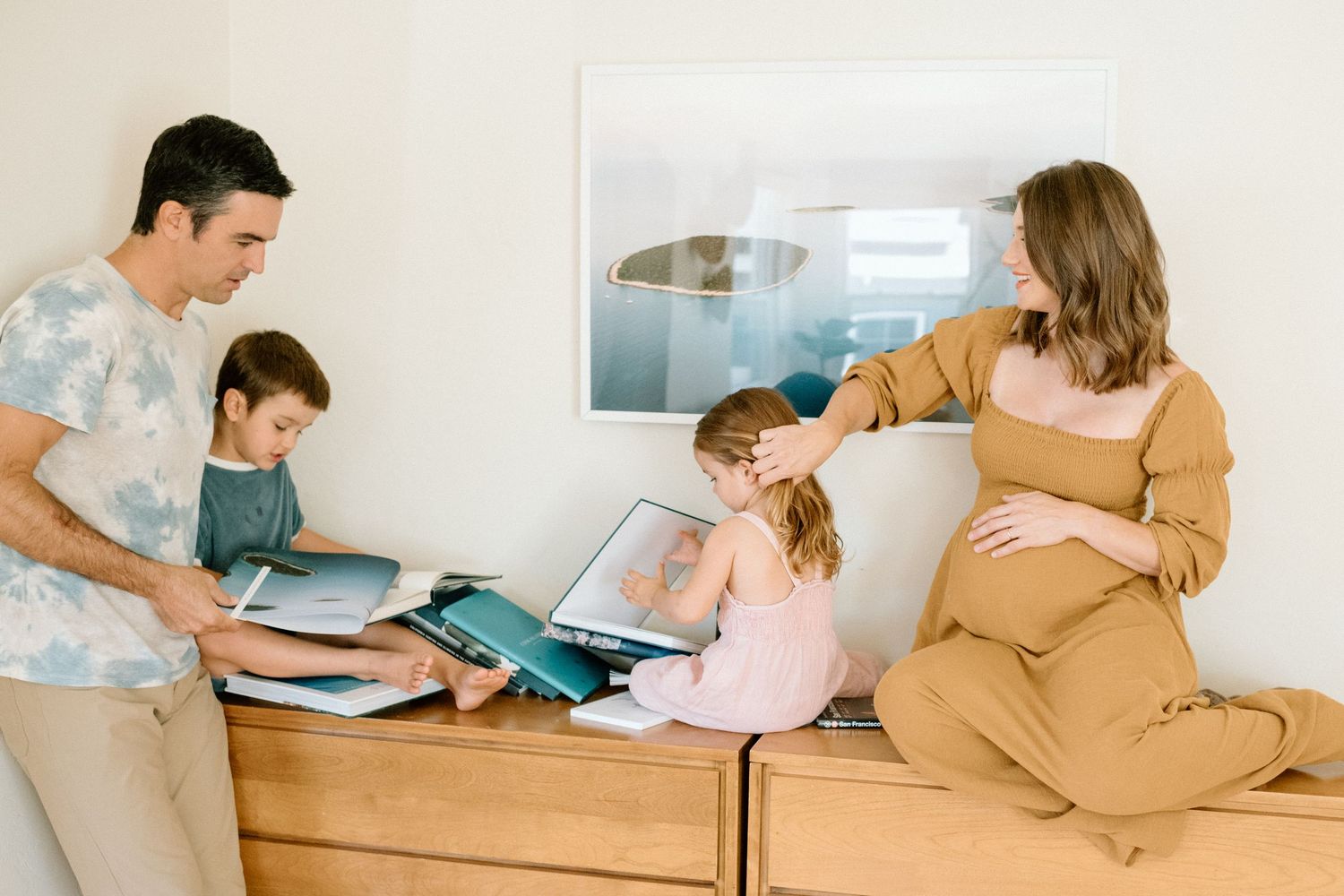 Family of four gathered around a wooden dresser, looking at books and photos together in a cozy home.
