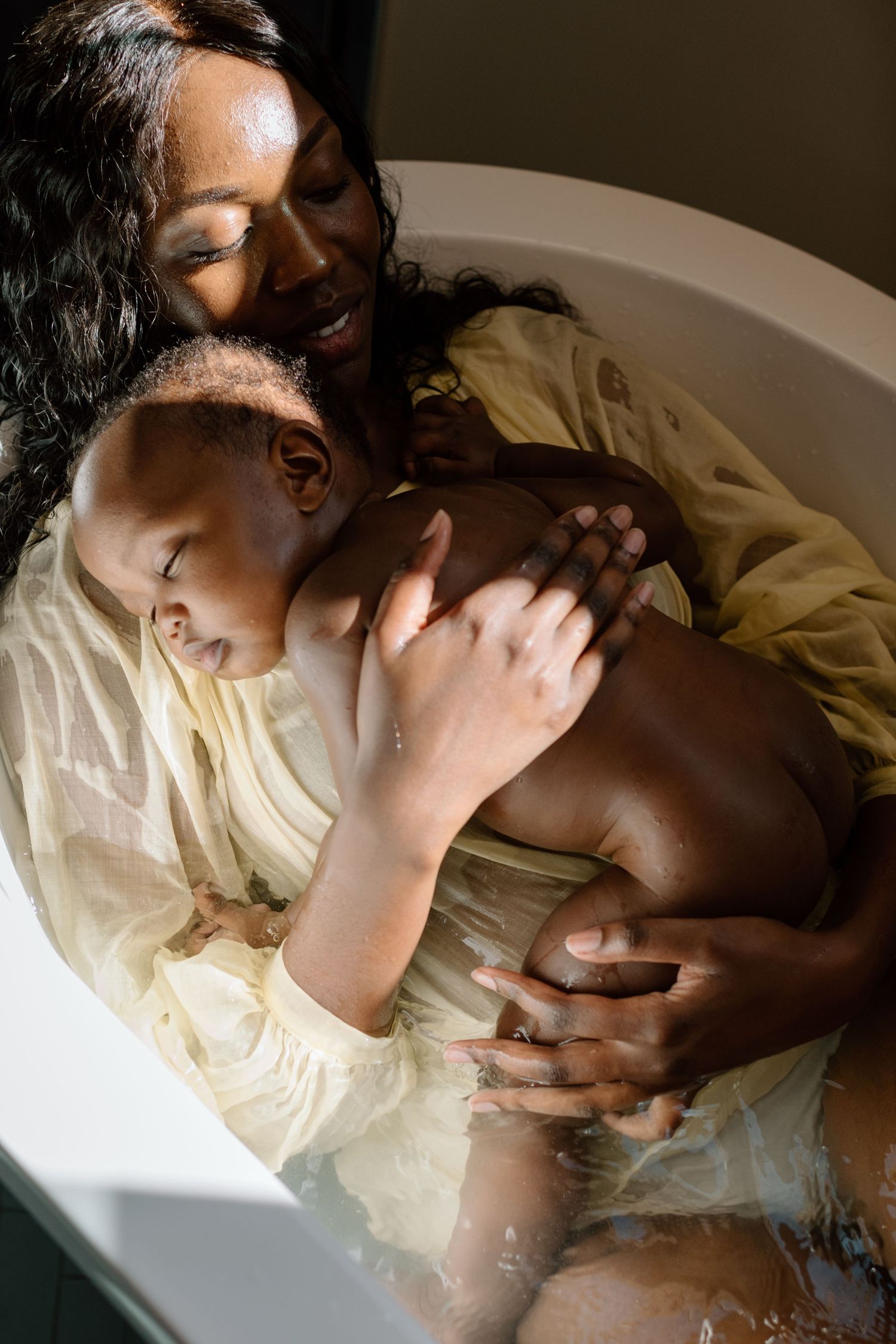 African American mother bathing with her young child in a sunlit bathtub.