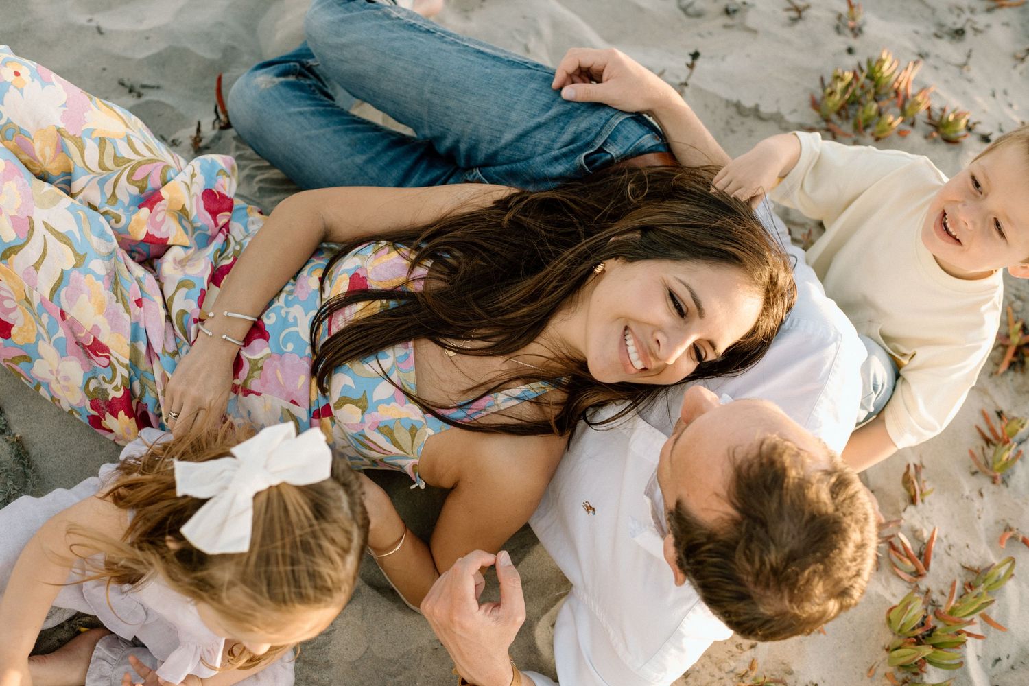 An aerial view of a joyful family cuddling together on the sand at the beach.