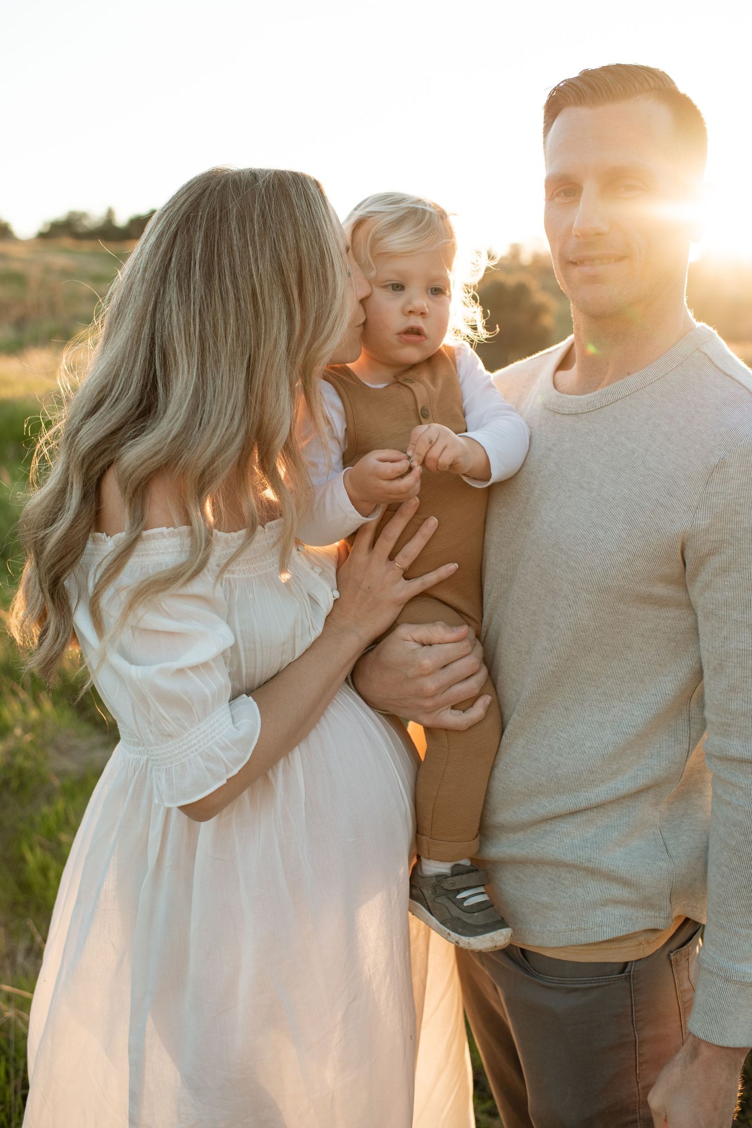 Happy family with pregnant mother, father, and toddler posing together in golden sunset light.