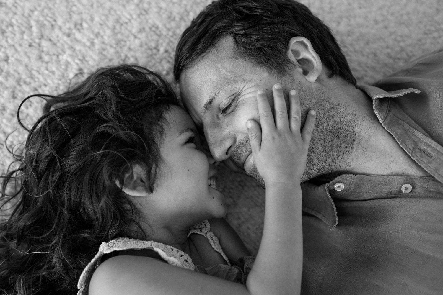 Black and white intimate moment of young girl touching fathers face as they smile at each other.