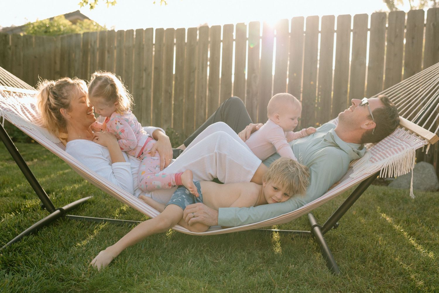 Happy family with three children relaxing together on a hammock in sunny backyard.