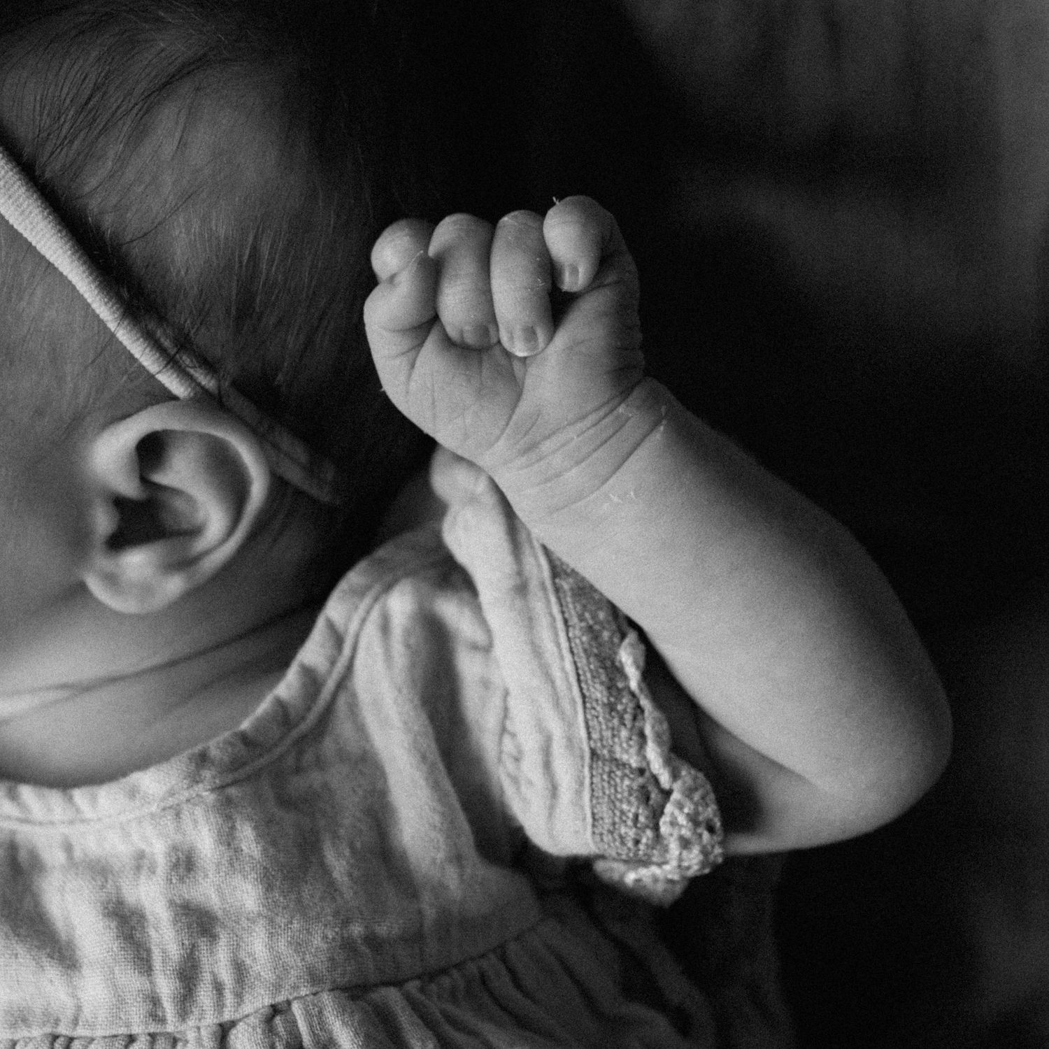 Black and white close-up photo of a sleeping newborn baby with tiny fist raised near face.