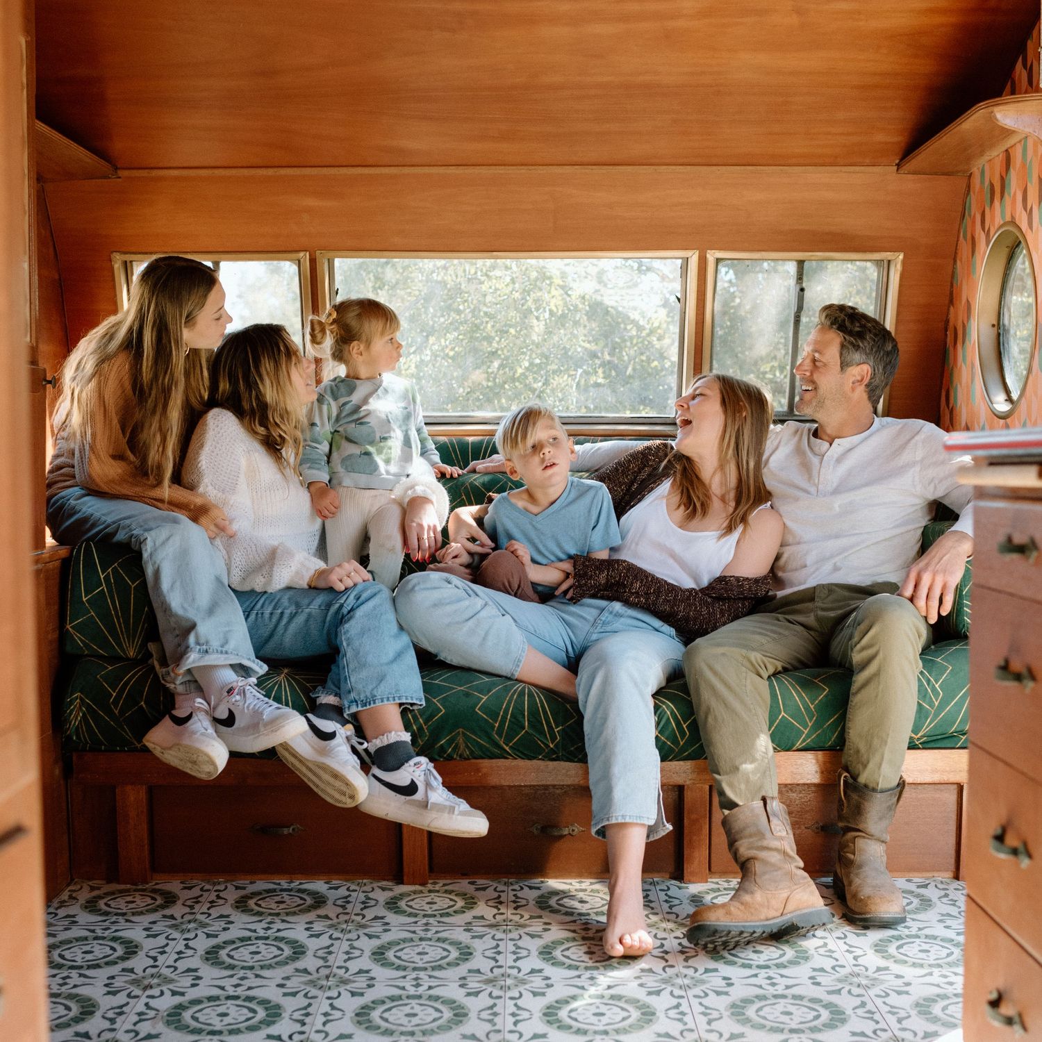 A happy family of six laughs and cuddles together on a built-in bench inside a vintage camper.