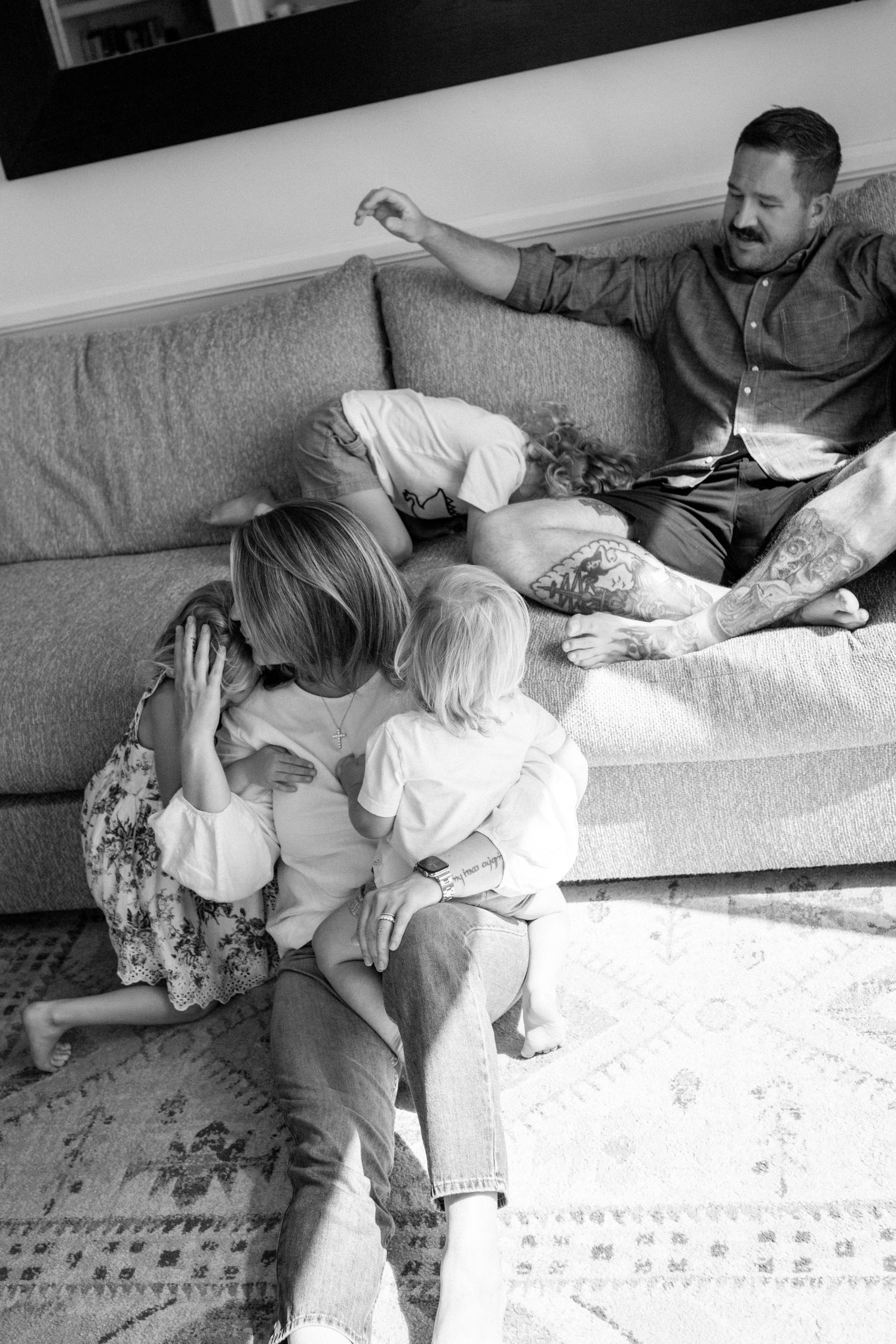 Black and white photo of a relaxed family with two kids lounging together on a living room couch.