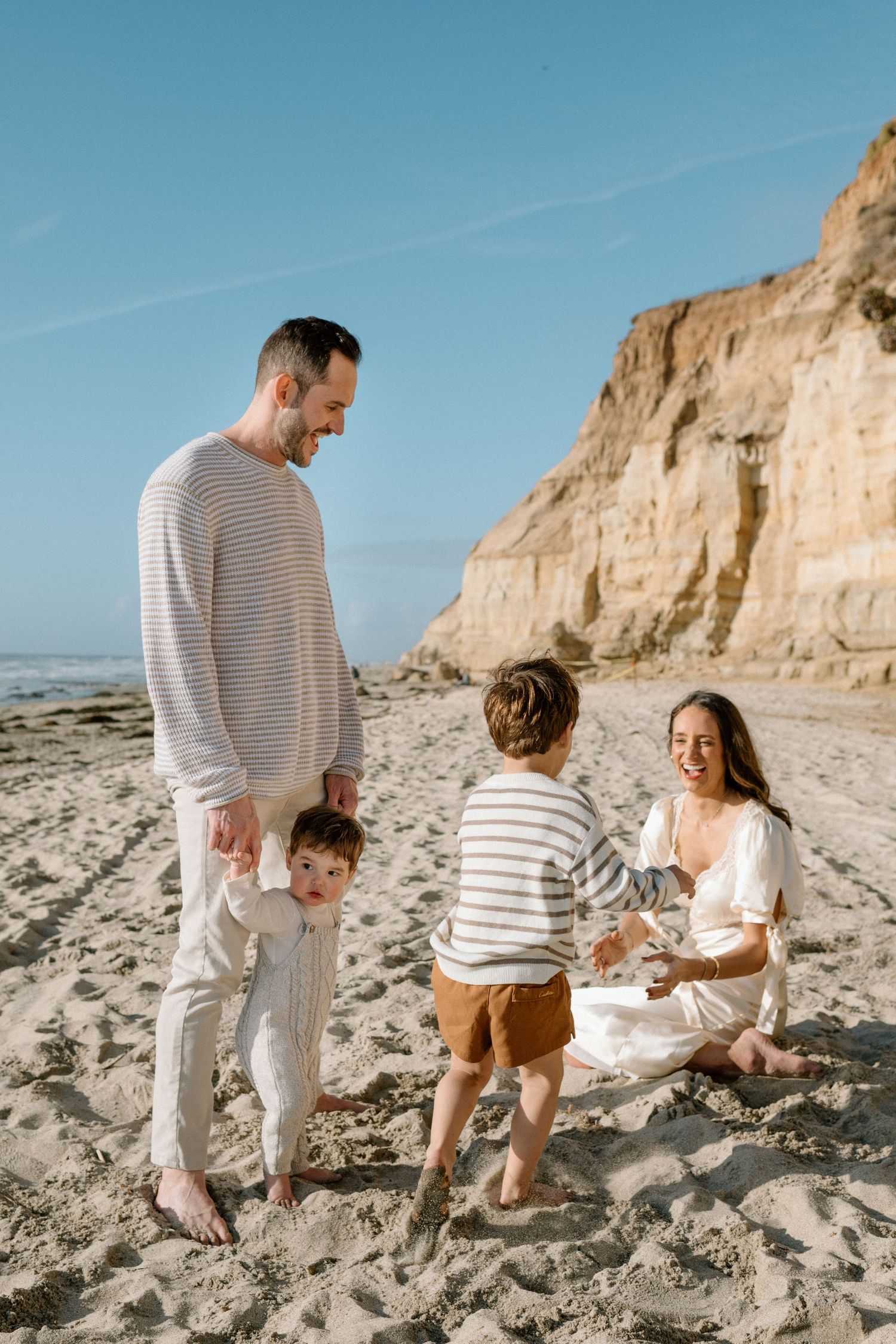 Happy family with two young children playing on a sandy beach near cliffs.