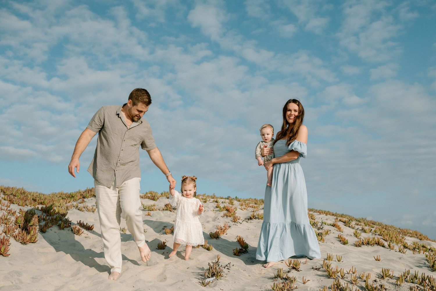 Young family walking on sandy beach dunes under cloudy sky.