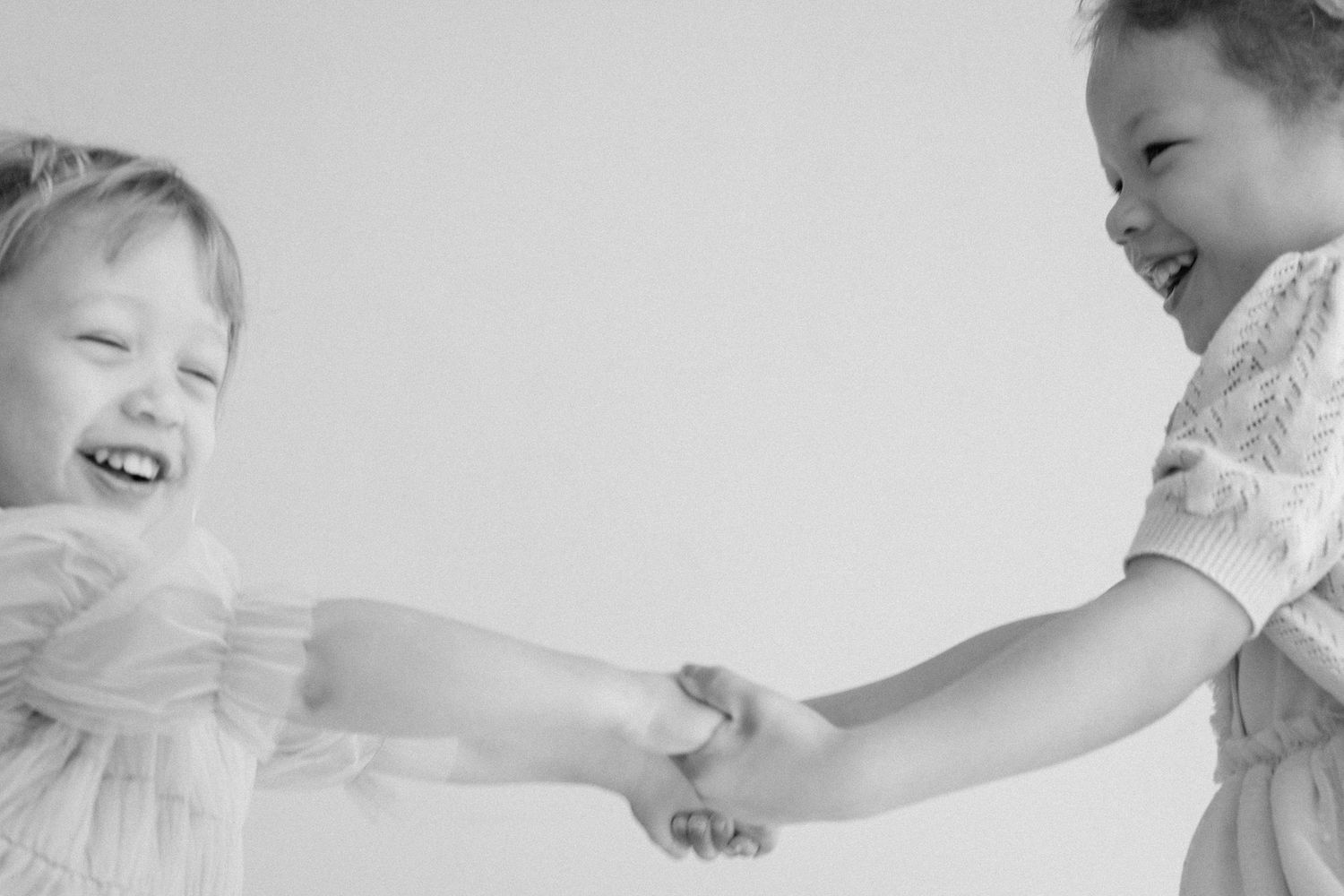Two young girls laughing and holding hands in a joyful black and white portrait photo.